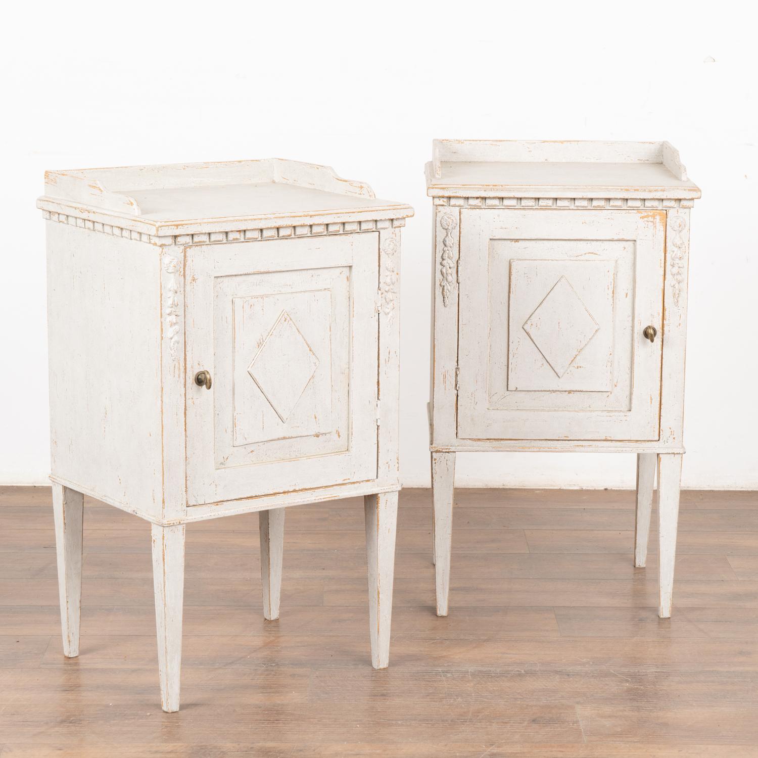 Pair, small Swedish country Gustavian white painted nightstands or side tables standing on tapered legs.
Applied floral carving accents the front along with dentil molding and diamond on panel door which opens with turning brass knob.
Professionally