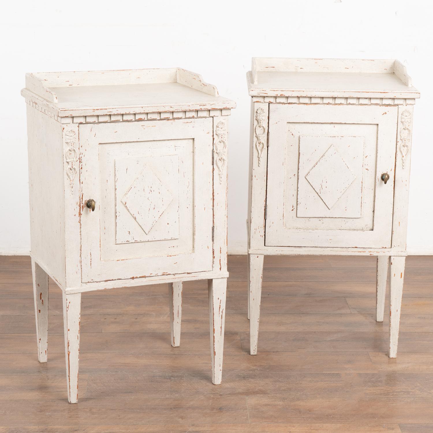 Pair, small Swedish Gustavian style white painted nightstands or side tables standing on tapered legs.
Applied floral carving accents the front along with dentil molding and diamond on panel door which opens by turning brass knob.
Professionally