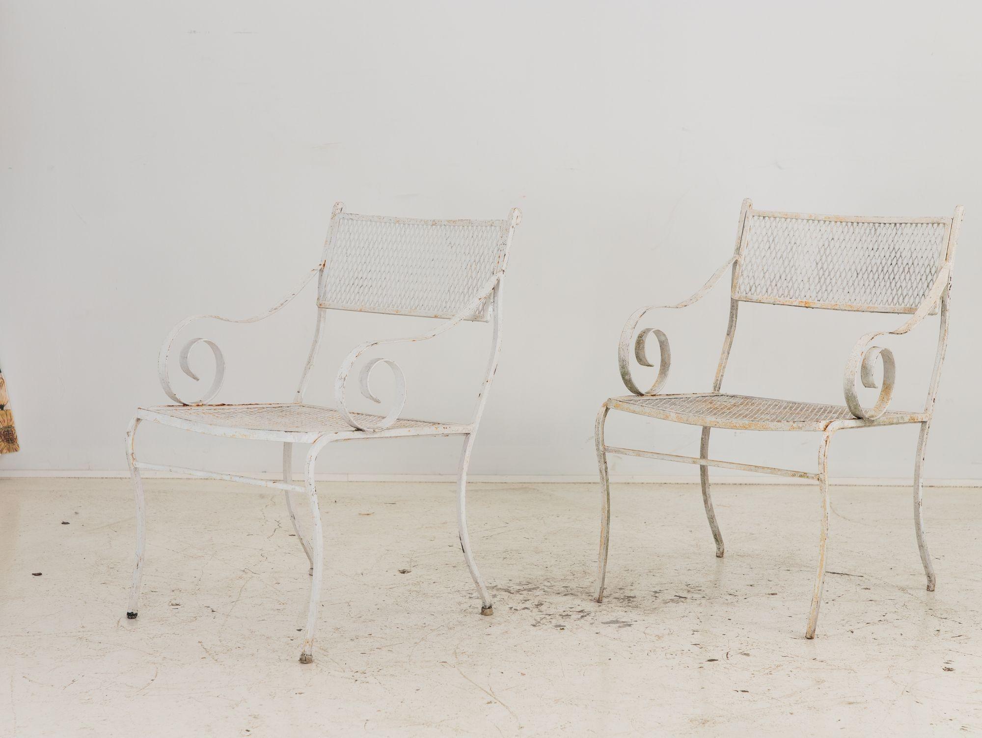 Crafted in the vibrant era of 1950s America, this pair of white-painted iron chairs embodies classic elegance and enduring style. With gracefully scrolled arms and splay legs, they exude sophistication reminiscent of the iconic designs of Woodard