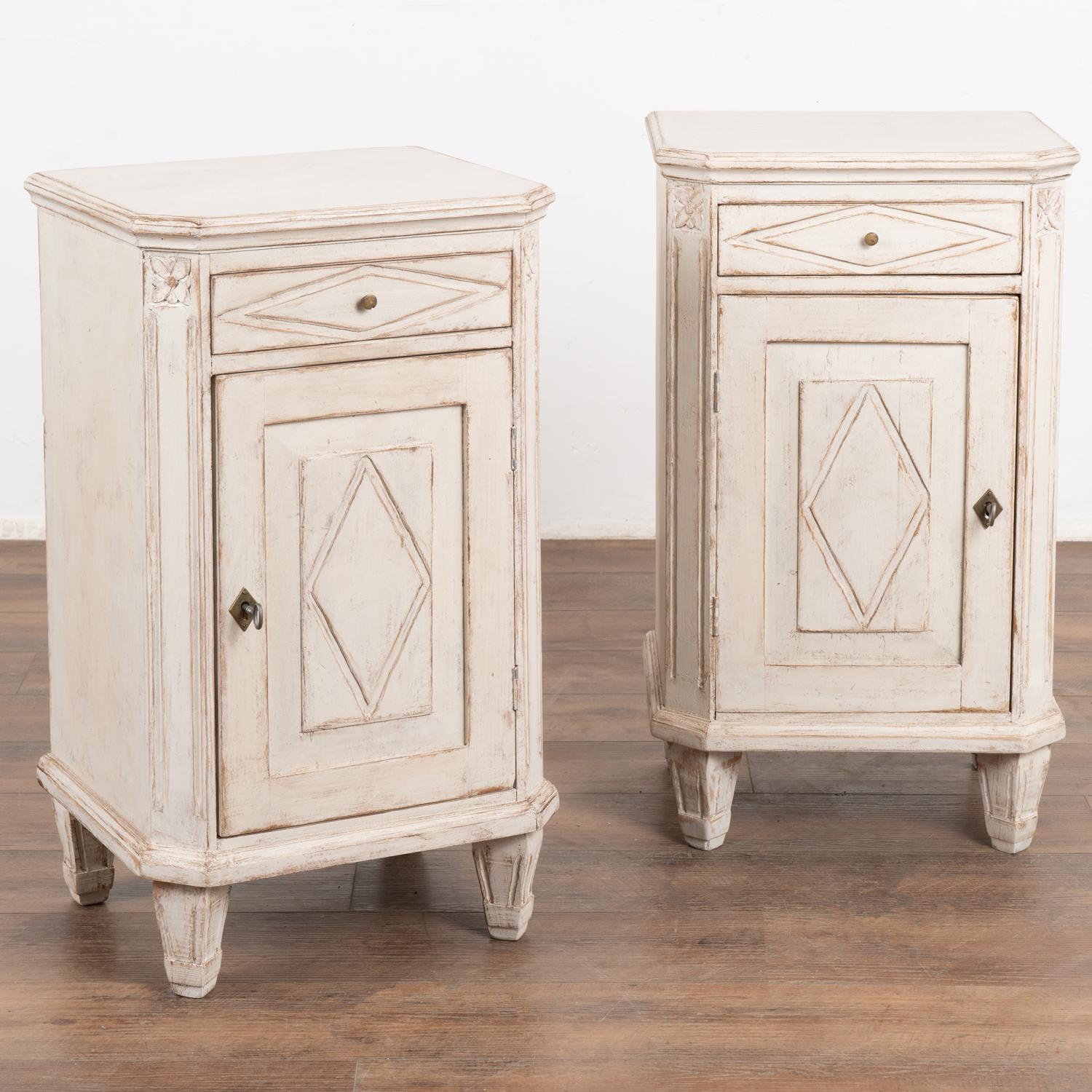 Pair, small Swedish country Gustavian style white painted nightstands or small cabinets standing on tapered feet.
Traditional diamond motif on doors and drawers, simple fluted carving along sides.
Newer professionally applied antique white painted