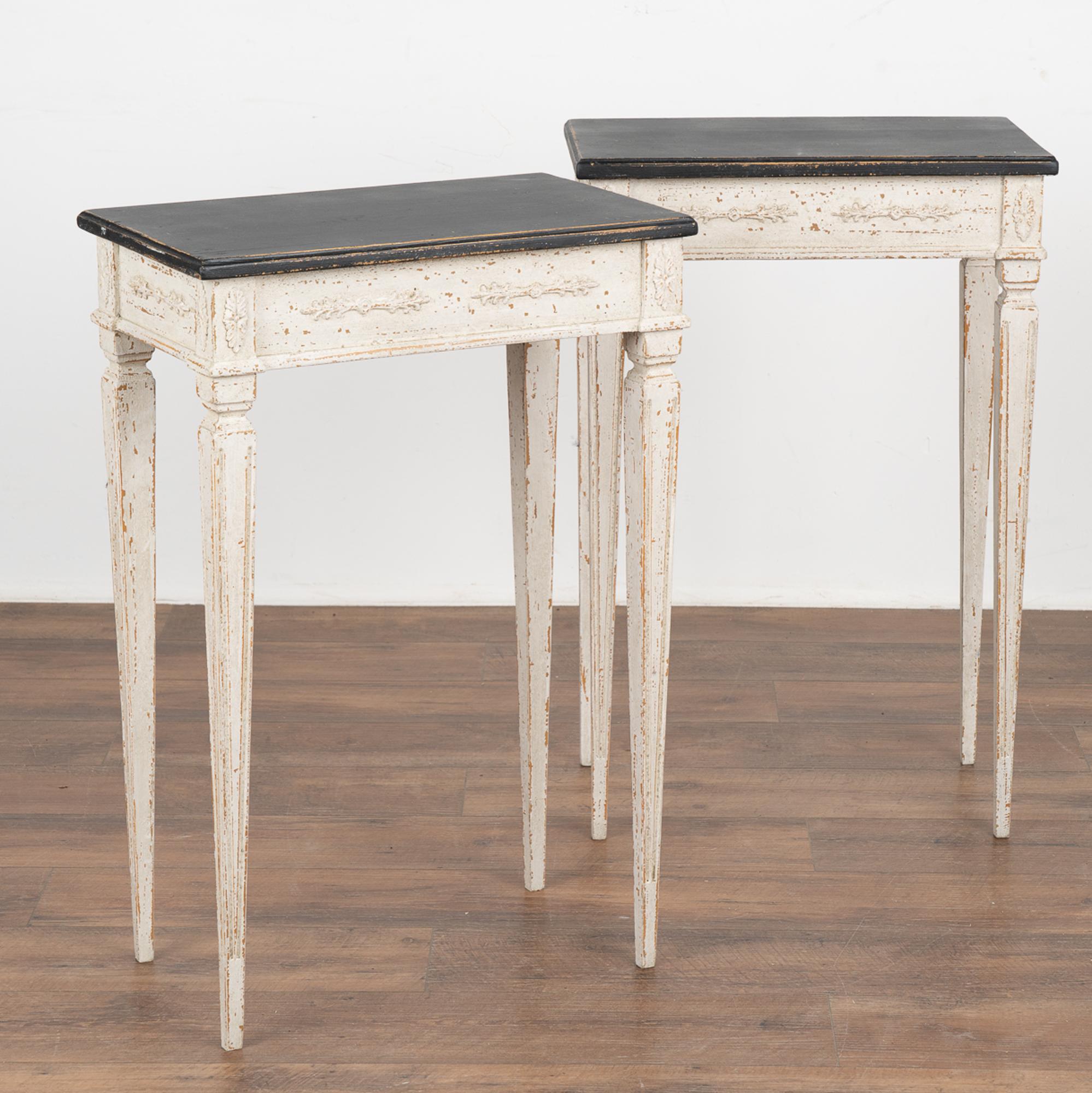 Pair, lovely white painted Swedish side tables resting on elegant narrow tapered and fluted legs.
The newer professionally applied layered white painted finish has contrasting black painted tops, slightly distressed to fit age and grace of the