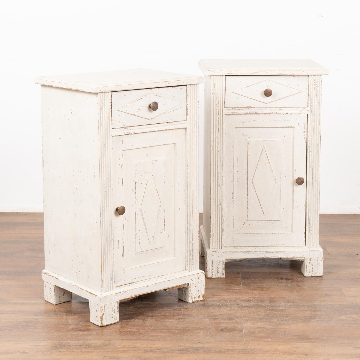 Pair, small Swedish country Gustavian style white painted nightstands or small cabinets standing on block feet.
Traditional diamond motif on doors and drawers, simple fluted carving along sides.
Newer professionally applied antique white painted