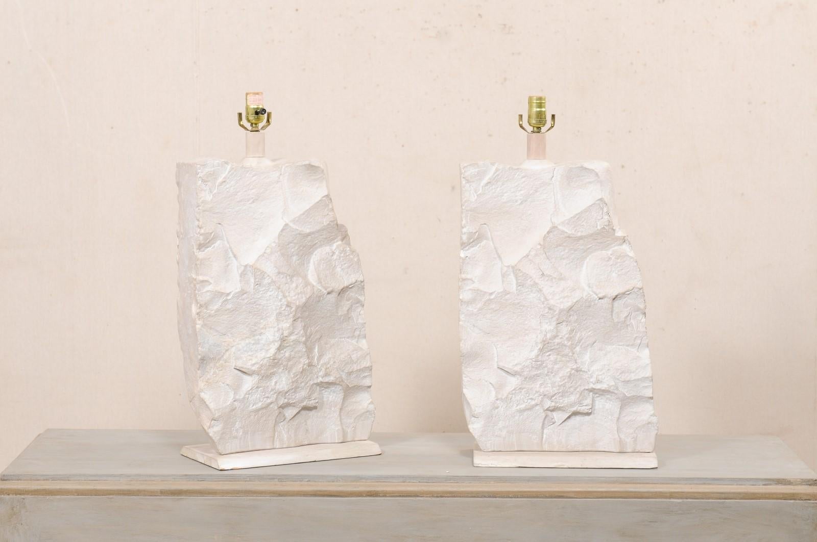 A pair of vintage American plaster table lamps attributed to Sirmos, though markings. This pair of plaster table lamps each feature a modern, quarry rock or brutalist design. The lamp bodies are made of plaster, have a neutral white and cream