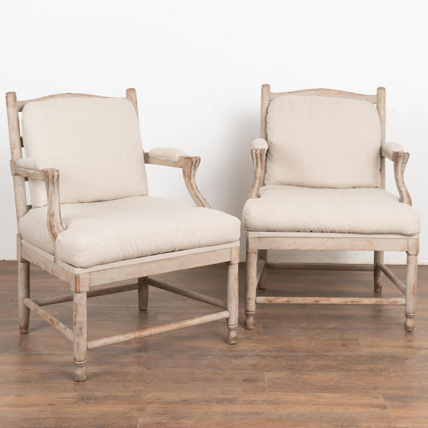This pair of Swedish country armchairs have padded arm rests and slat backs with cushions for back and seat.
The newer professionally applied antique white layered painted finish has been gently distressed fitting the age and grace of the pair.
Wood
