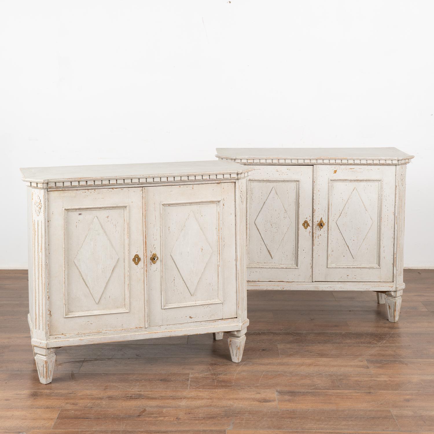 Pair, Swedish country pine cabinets or small sideboards with canted fluted sides, dentil molding and carved diamond motif on doors.
The newer, professionally applied antique white custom painted finish is perfectly distressed to fit the age and