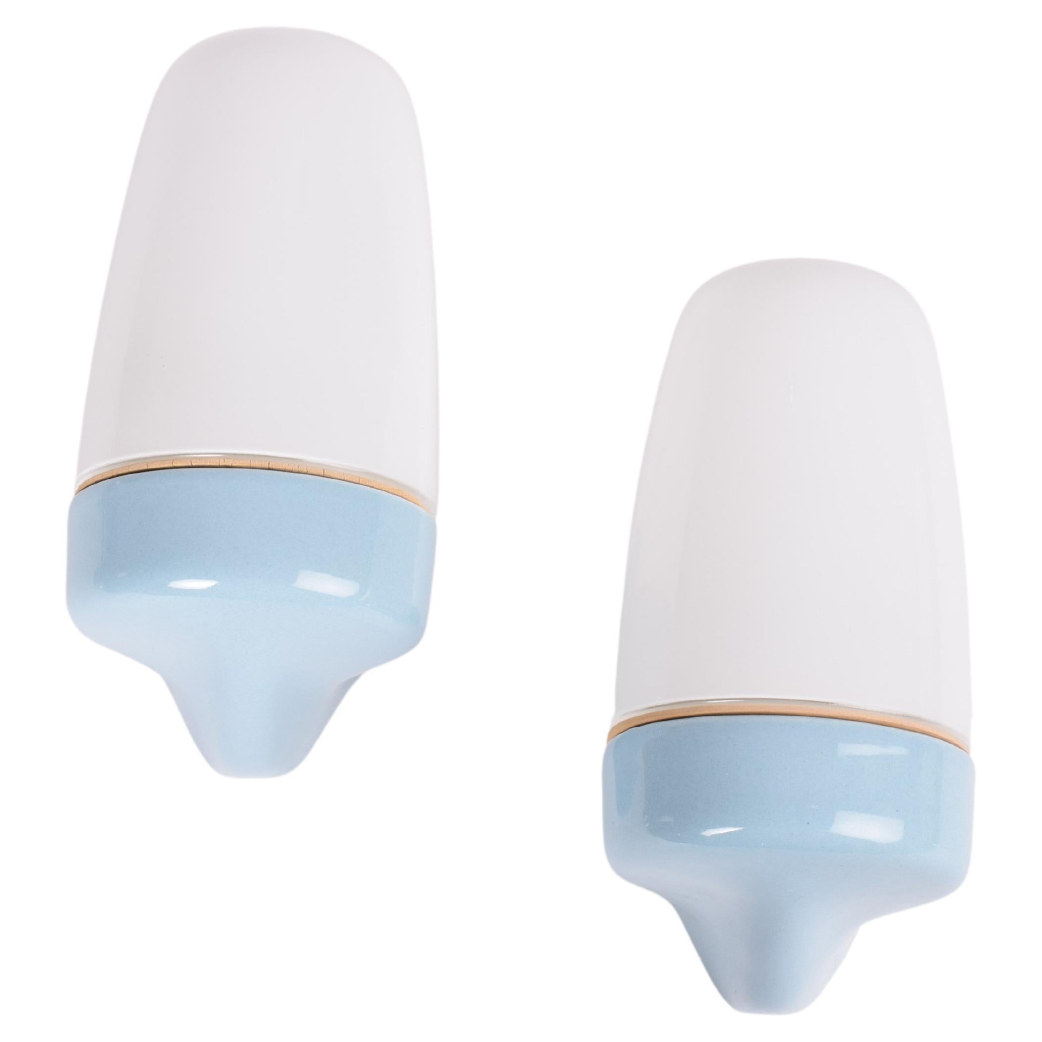 Set of two original vintage wall sconces by German designer Wilhelm Wagenfeld. They were manufactured by Lindner Wandleuchten ca 1950s.

This set has baby blue glazed ceramic holders with white opaline glass bulb covers.
Both the model and the