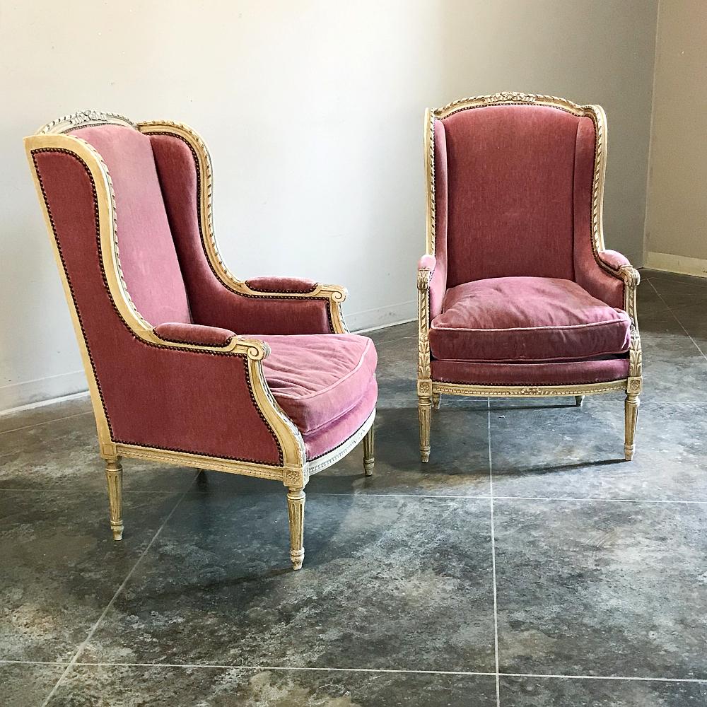 Pair of antique French Louis XVI painted Wingback bergères combine the light and airy look of hand carved and painted fruitwood with the wraparound luxurious comfort of the generously sized wingback design to create the perfect seating group in any