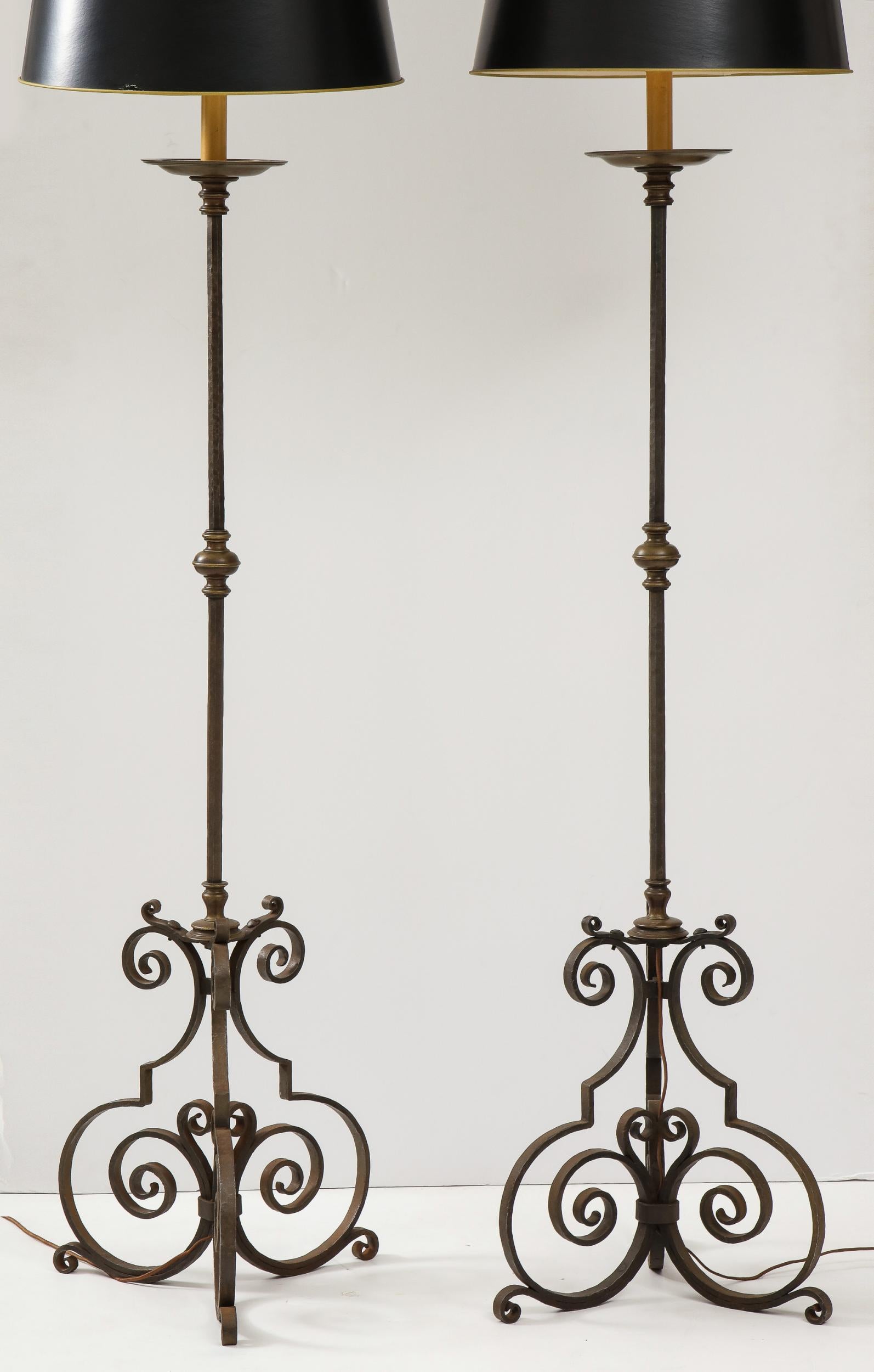 Good pair of Early 20th century wrought iron and brass standard lamps having hand hammered shafts, bronze drip pans and collars and standing on scrolled legs, nicely patinated and of good scale.