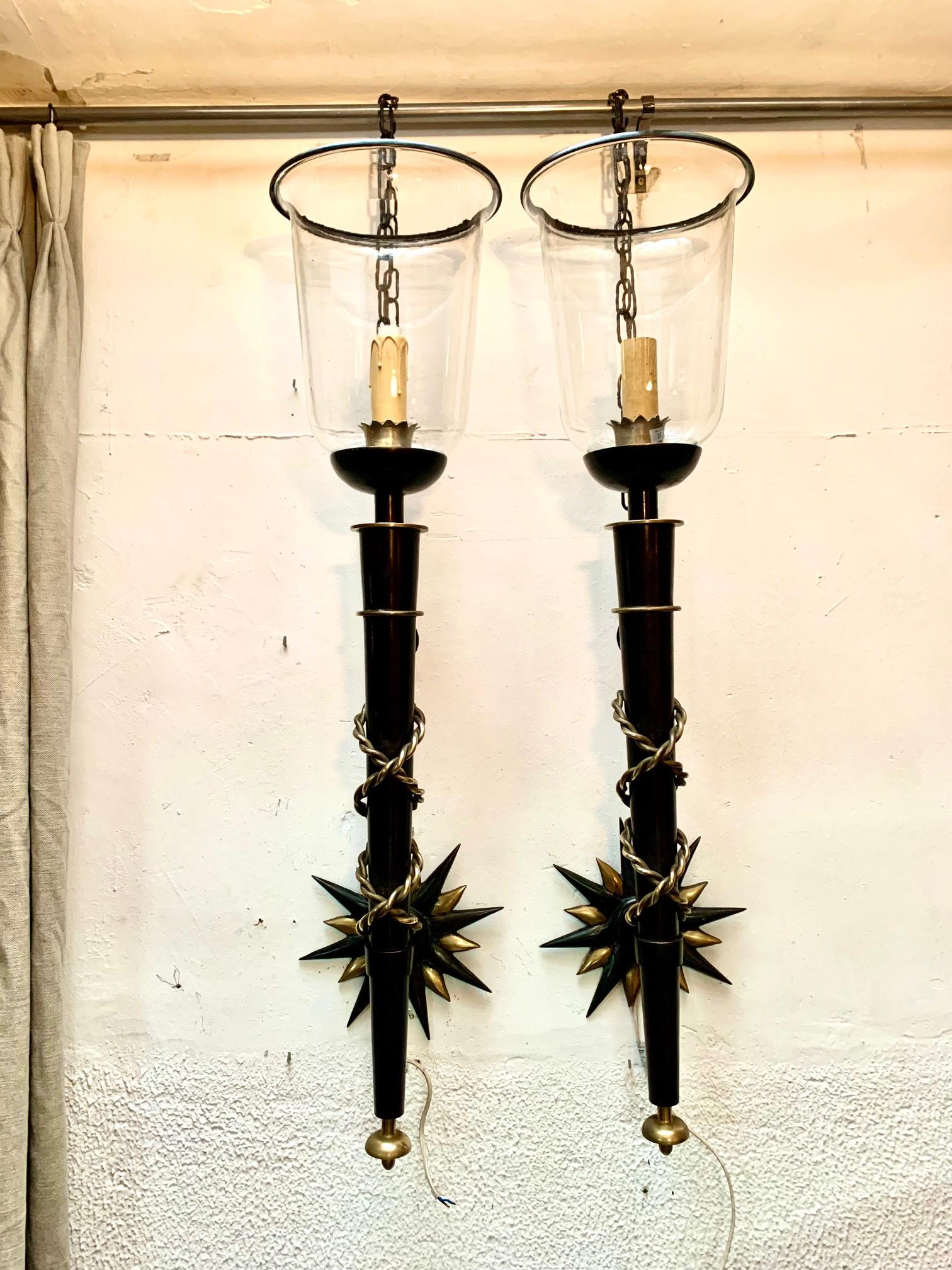 A pair of important and large torch-shaped wall sconces, these sconces follow the unmistakable style of Gilbert Poillerat, they are made of wrought iron and lacquer, combined with many other details in brass and bronze, The sconces rest on the wall