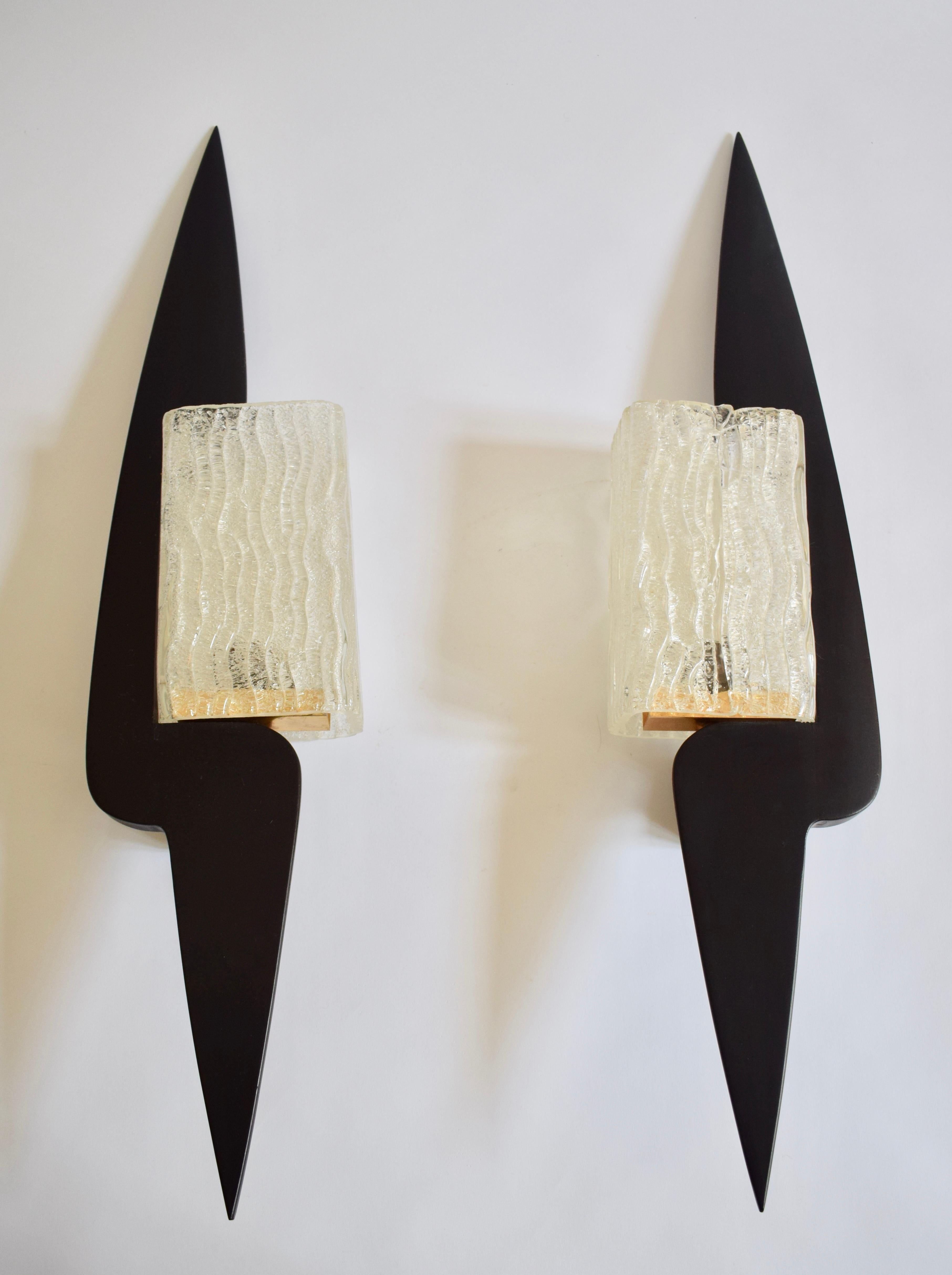 Rare paire d'appliques Arlus en bois laqué noir et verre. Forme graphique élancée dans laquelle s'inscrit un abat-jour rectangulaire en verre granité à motifs de vaguelettes. Travail réalisé dans les années 1960. Système électrique fonctionnel.