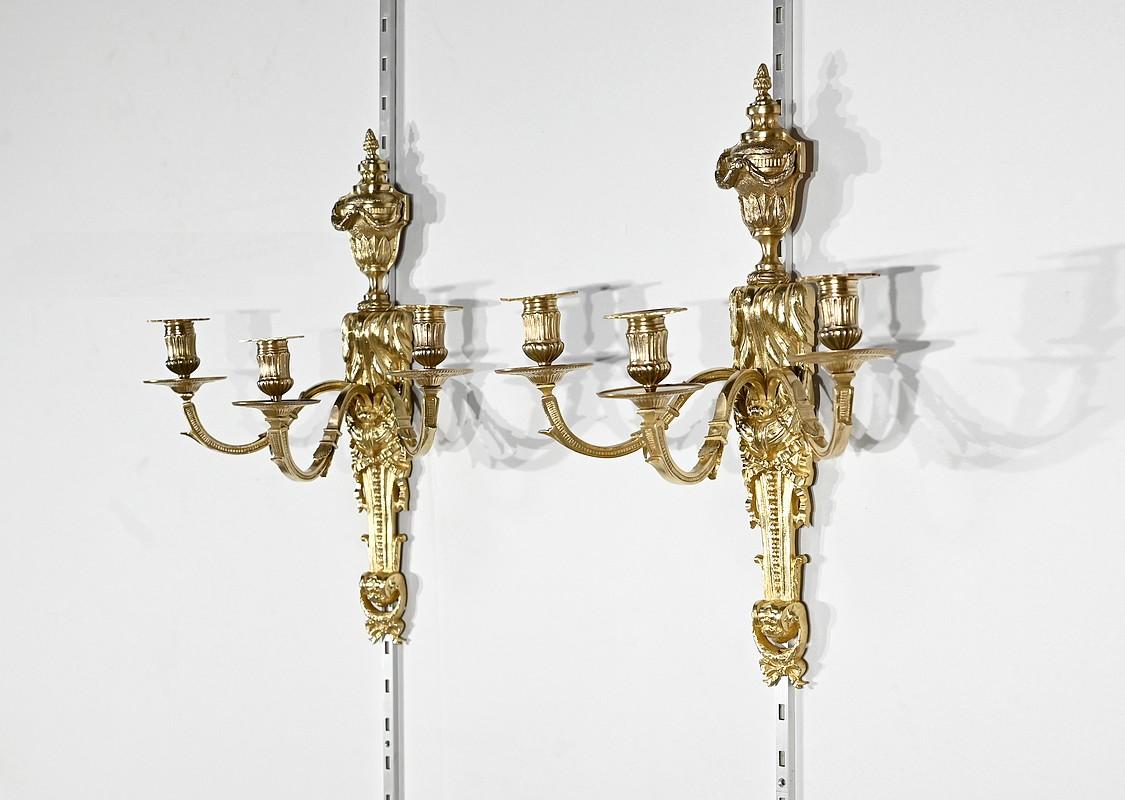 Magnifique ensemble d'appliques en bronze doré à trois bras de lumière présentant une ornementation de style Louis XVI.
Ces appliques comportent une partie murale représentant une urne entourée d'une épaisse guirlande de feuillage et surmontée d'une