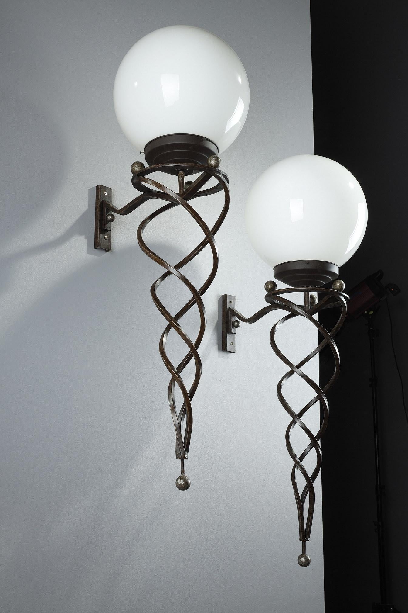 Pair of wrought iron sconces in the Art Deco style from the late 20th century. Each light fixture is composed of a shaft in twisted swirling rods giving movement and lightness to the whole. The wrought iron structure raises a spherical shade in