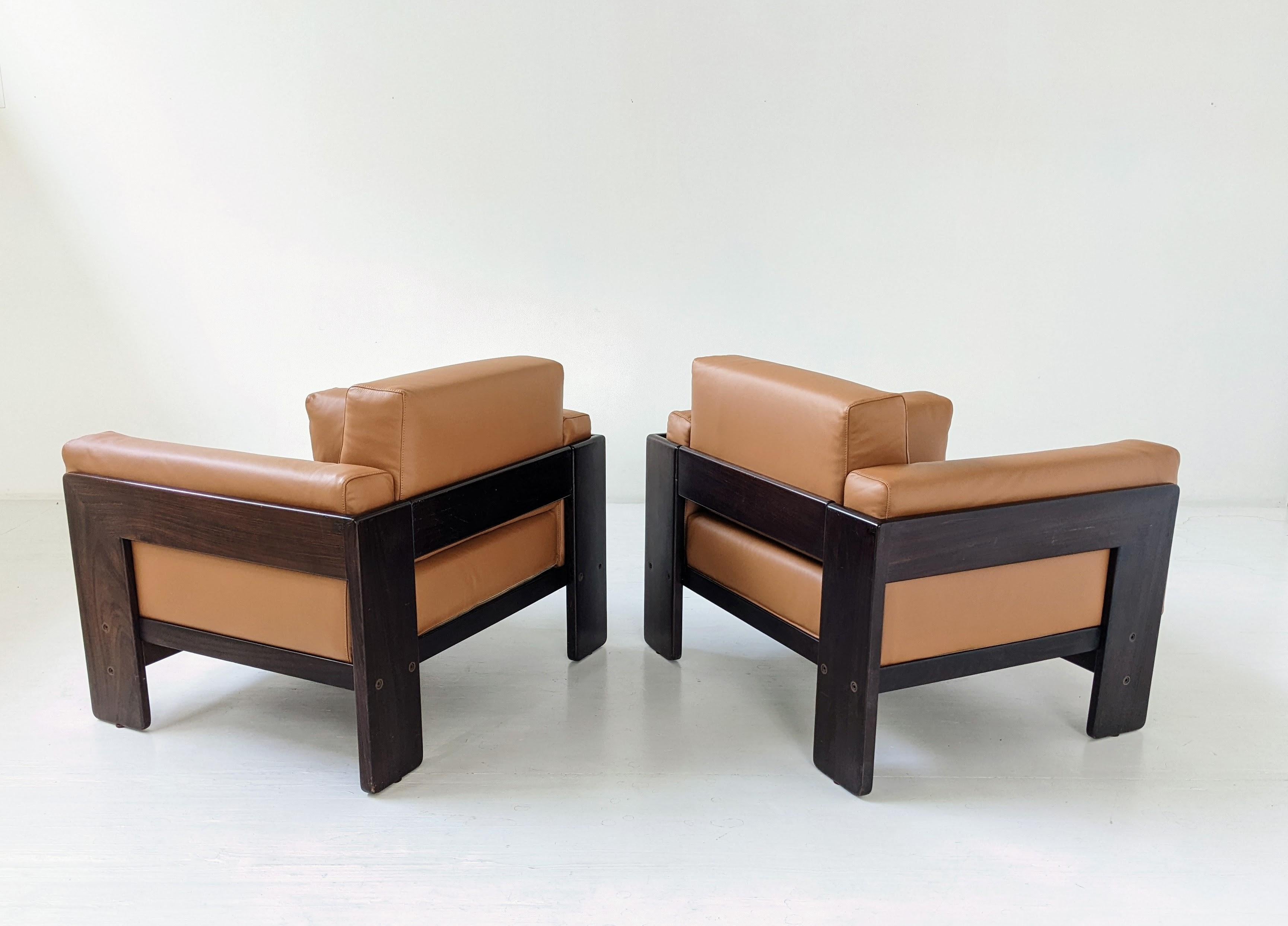 Paire de fauteuils Bastiano réalisé avec une structure en bois et des coussins en cuir brun cognac. Tobia Scarpa a conçu la série Bastiano pour la maison d’édition Gavina en 1960. Très confortable, les coussins sont très épais et sont maintenus par