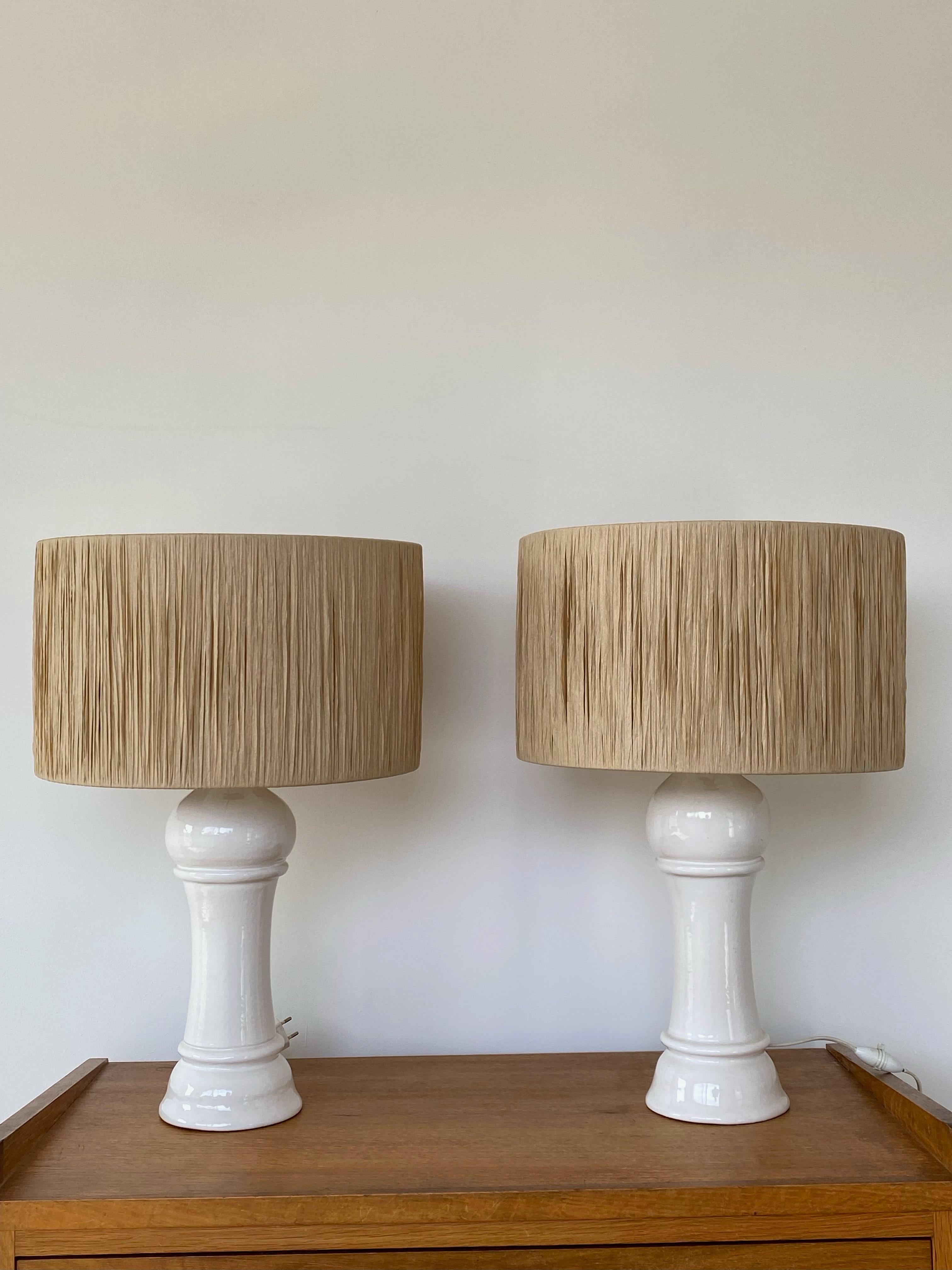 Rare pair of table or bedside lamps, ceramic, height 40 cm.
 Off-white enamelled ceramic, of Italian origin, signature to be identified.
 Mounted with a raffia lampshade (recent production), 40 cm in diameter and 20 cm in height.
 Realization very