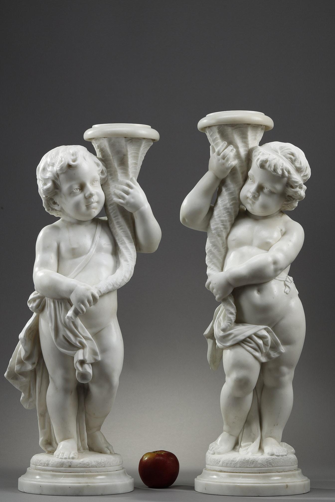 Pair of sculptures in white Carrara marble, made in Italy at the end of the 19th century. These mythological statuettes represent two putti holding in their hands a cornucopia in the shape of a triton shell. Each putto, wrapped in a drape, stands in