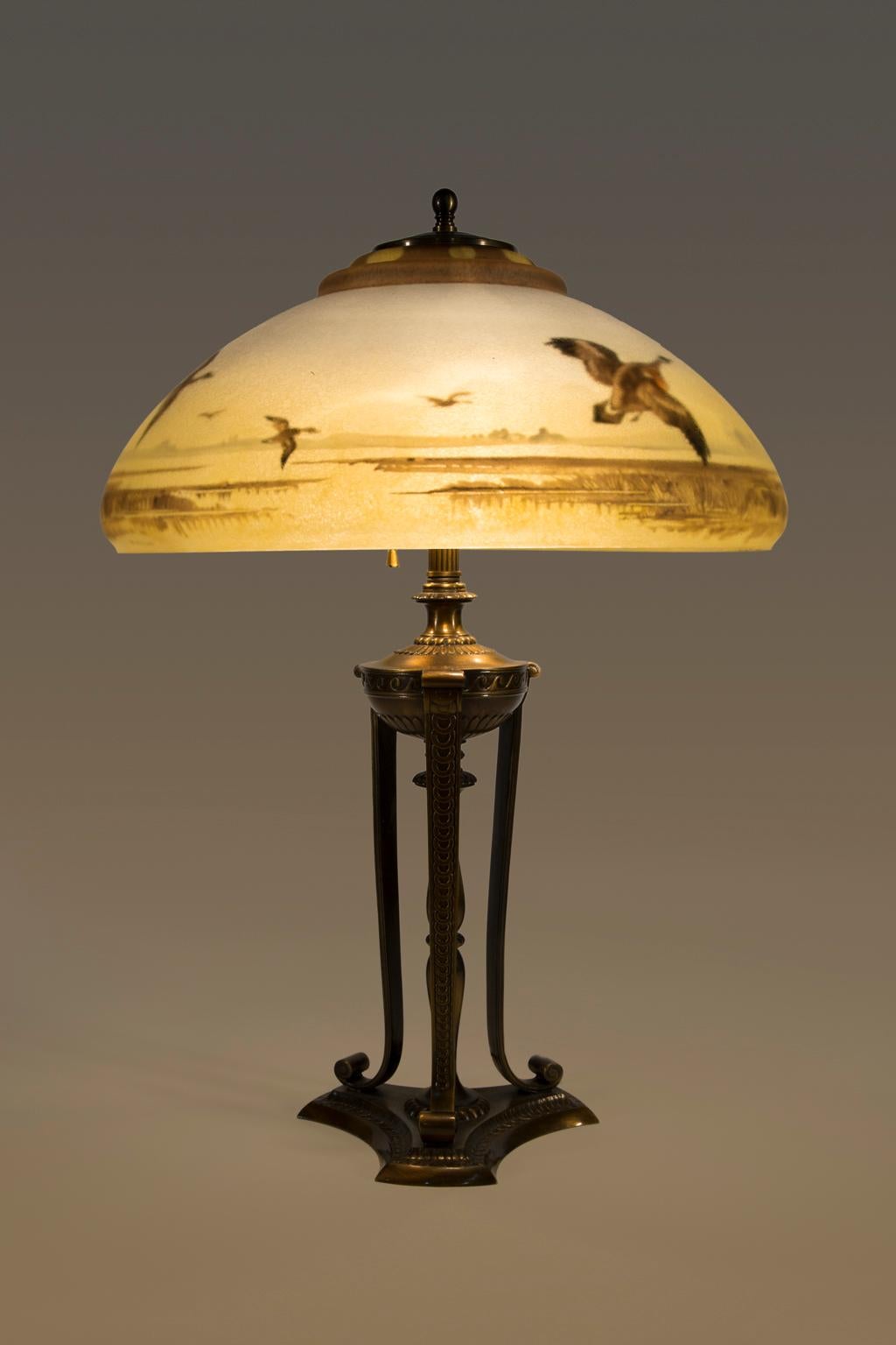 SALE ONE WEEK ONLY

This is a beautiful brass and glass lamp with a flock of geese in flight over a water landscape. Shading of sky has the soft blue and golden color of an evening sunset. 

Pairpoint is known for three kinds of glass lampshades,