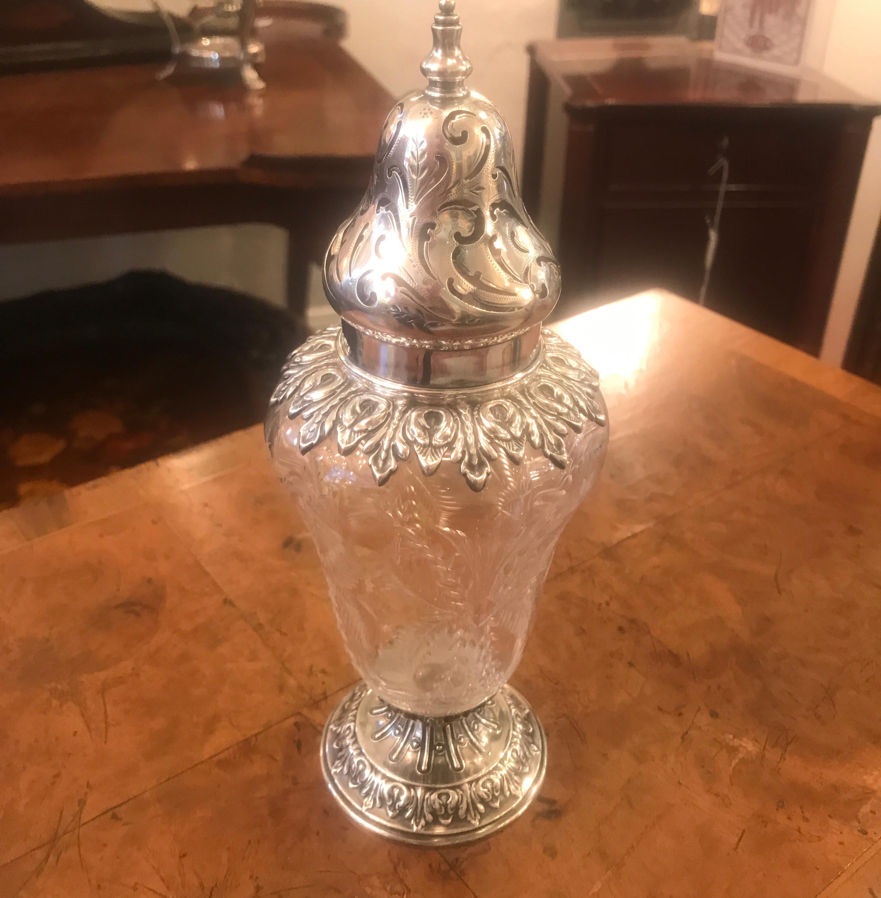 A sterling silver and intaglio cut class muffineer sugar shaker, 8.5 inches tall. The glass is cut with sprays of floral and foliat garlads and mounted in sterling silver on the top, bottom and cap.