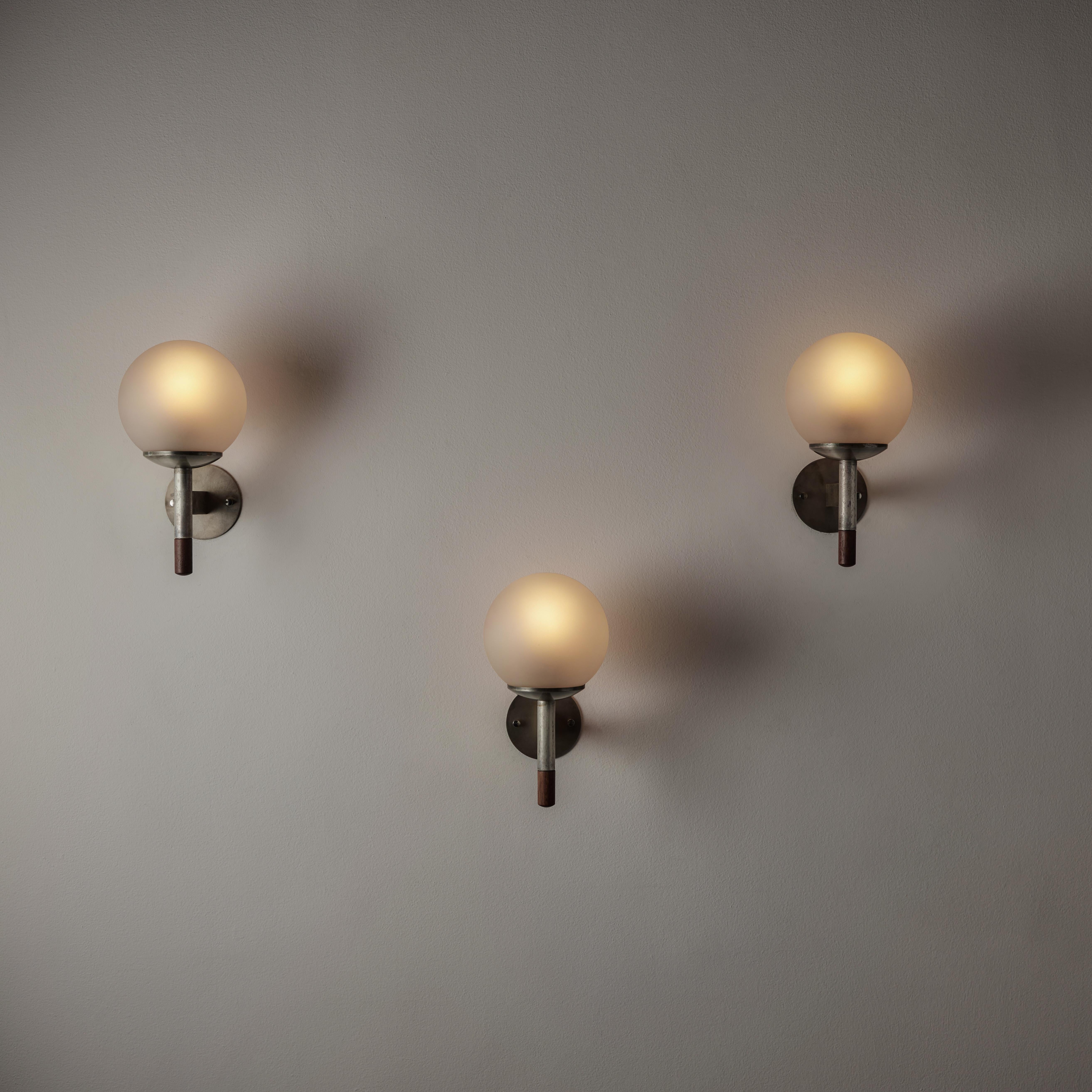 Pair of Arredoluce sconces. Designed and manufactured in Italy, circa the 1950s. Industrial metal stem wall lamps with underside teak caps. Lamps diffuse light through frosted globes that are centered on the metallic and wood torch stem. We