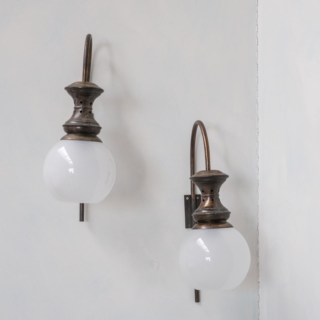 A pair of mid-century wall lights, in the manner of Caccia Dominioni. 

Italy, c1960s. 

Patinated brass and etched glass shades. 

Please note these are in vintage condition, there are small dings, slight bends in the curved necks of the