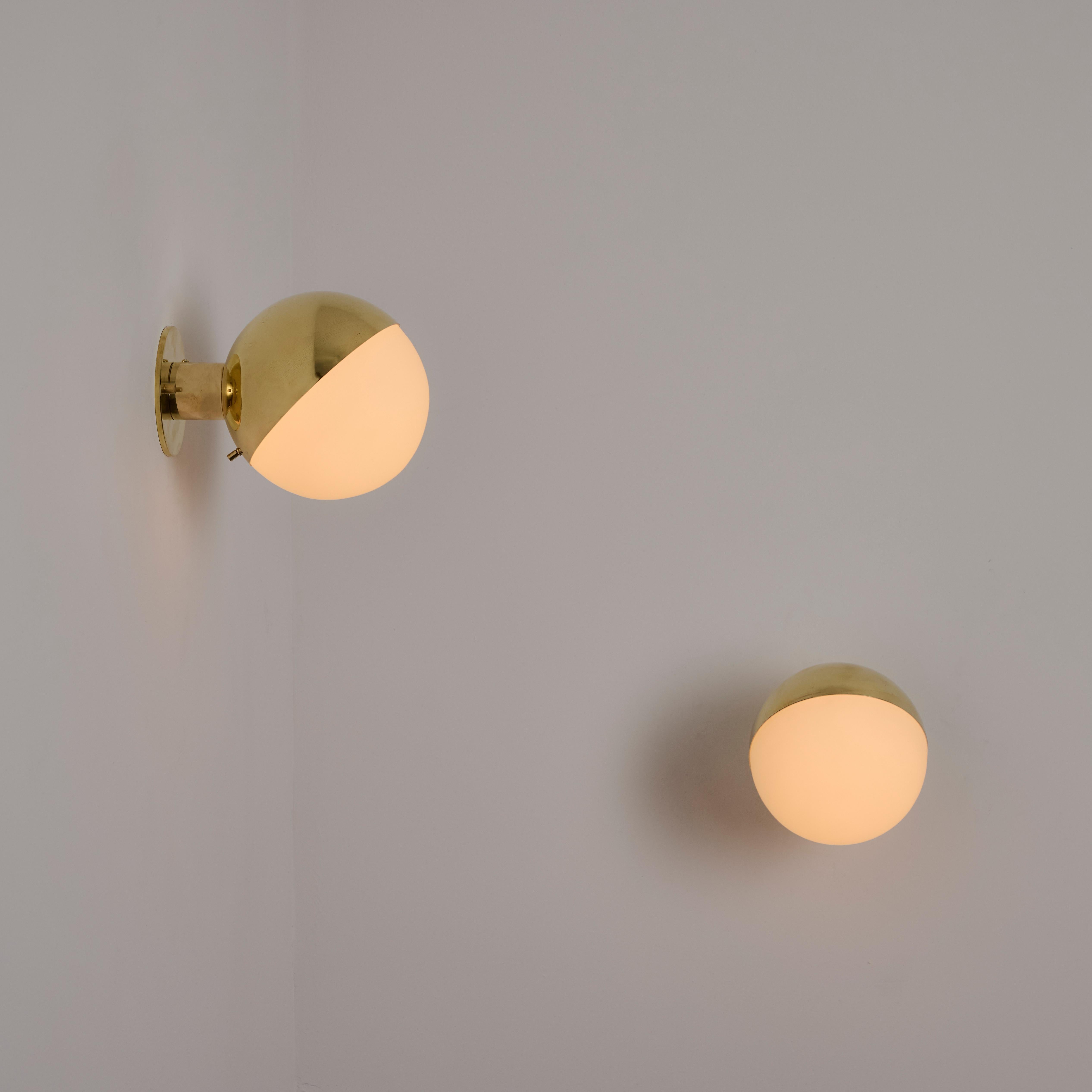 Appliques modèle 2045 de Stilnovo. Conçu et fabriqué en Italie, vers les années 1950. Une véritable approche minimaliste pour ces appliques boule simples mais saisissantes. Une armature en laiton et un demi abat-jour supérieur abritent un globe en