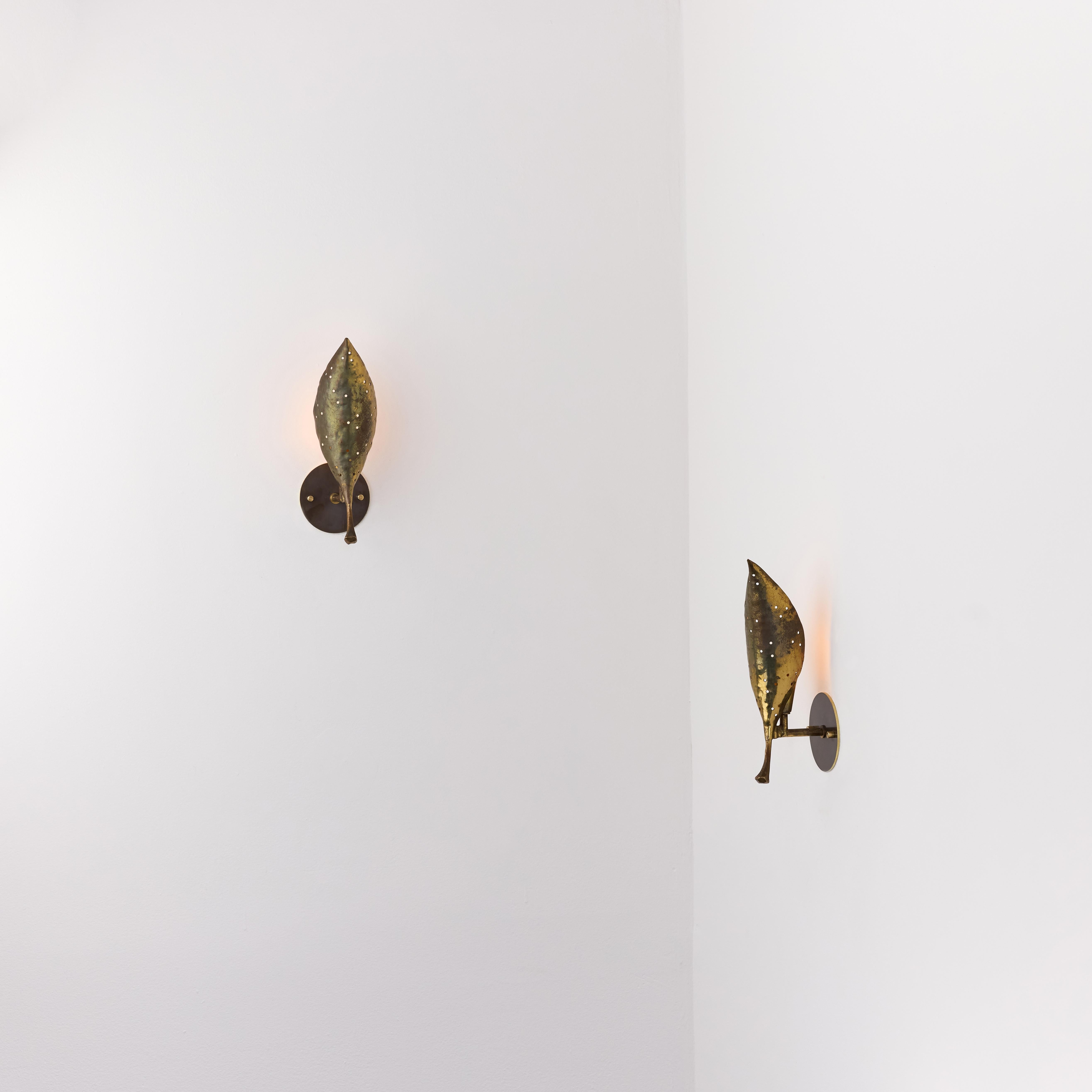 A Pair of Sconces by Angelo Lelii for Arredoluce. Designed and manufactured in Italy, circa the 1950s. All brass leaf formed shades with hammered detailing. The brass is heavily patinated and shows good signs of multiple lives. Shades can be pivoted