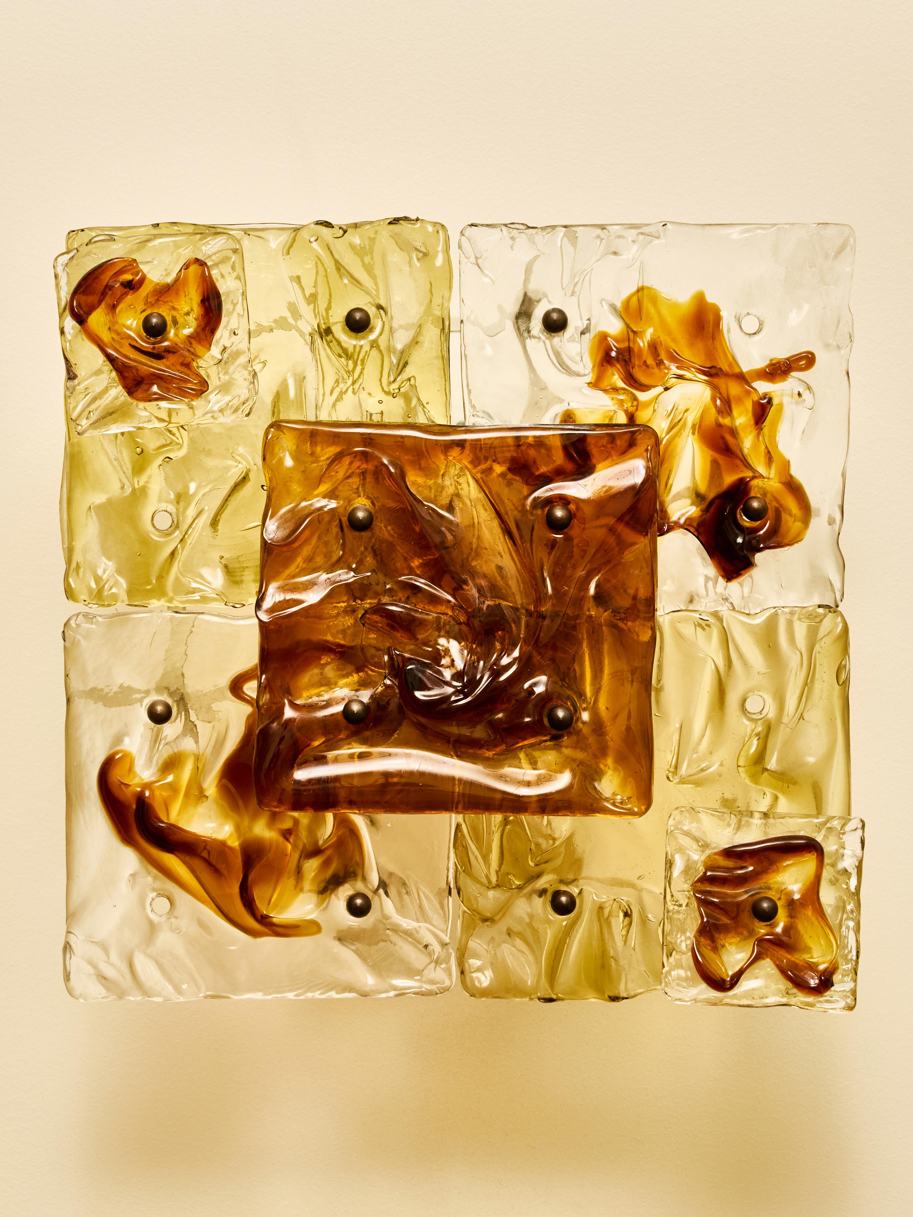 Coppia di applique scultoree disegnate da Toni Zuccheri per Venini negli anni Settanta. Ogni apparecchio è composto da piastrelle in vetro di Murano formate a mano e disposte in una griglia espressiva di elementi quadrati. Il vetro esibisce le