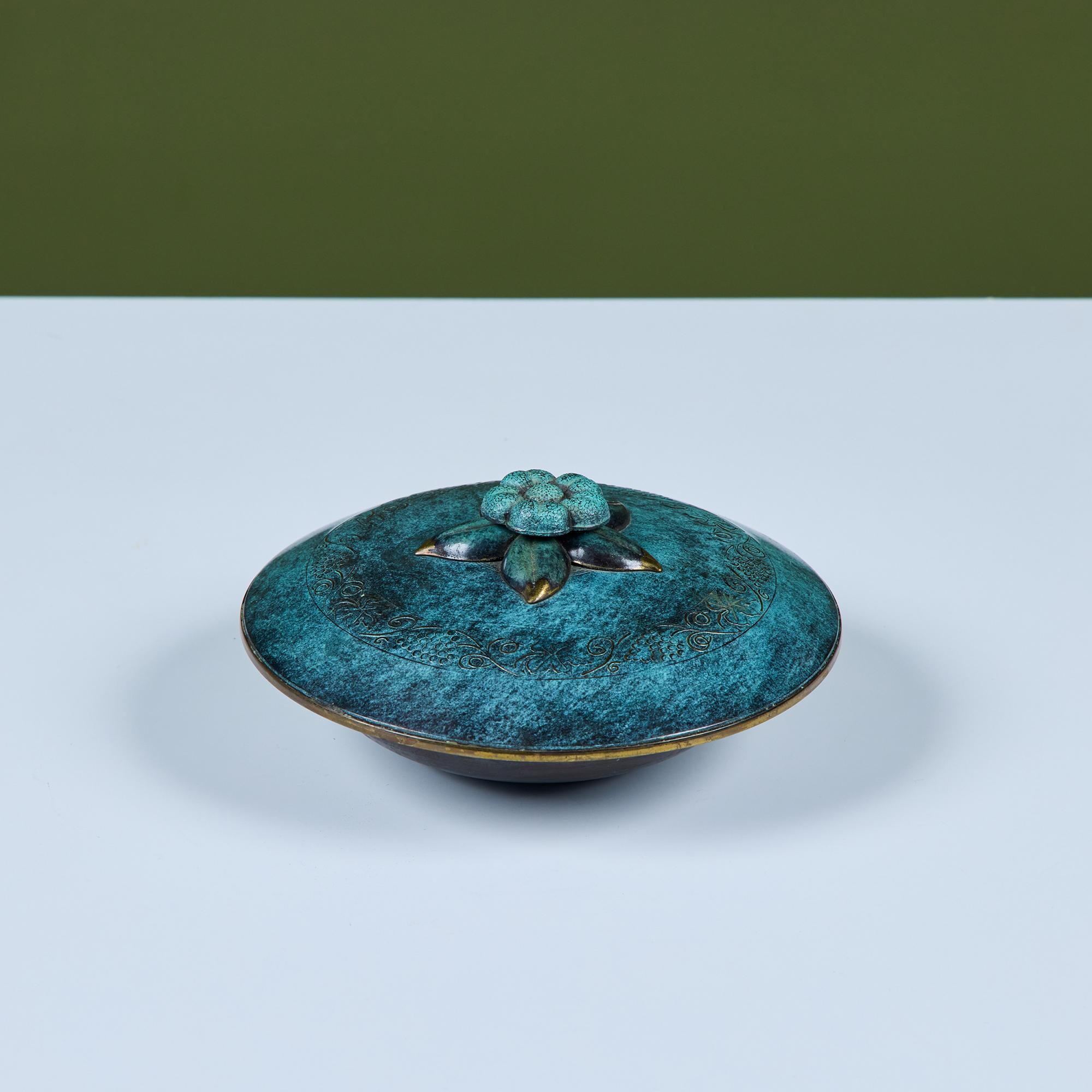 Bol redondo Pal-Bell con tapa. Esta pieza presenta un cuenco y una tapa de bronce verdigris con un pomo con detalles florales y puntas de latón. Perfecto para guardar llaves, joyas o popurrí. Un sello en relieve en la parte inferior del cuenco reza