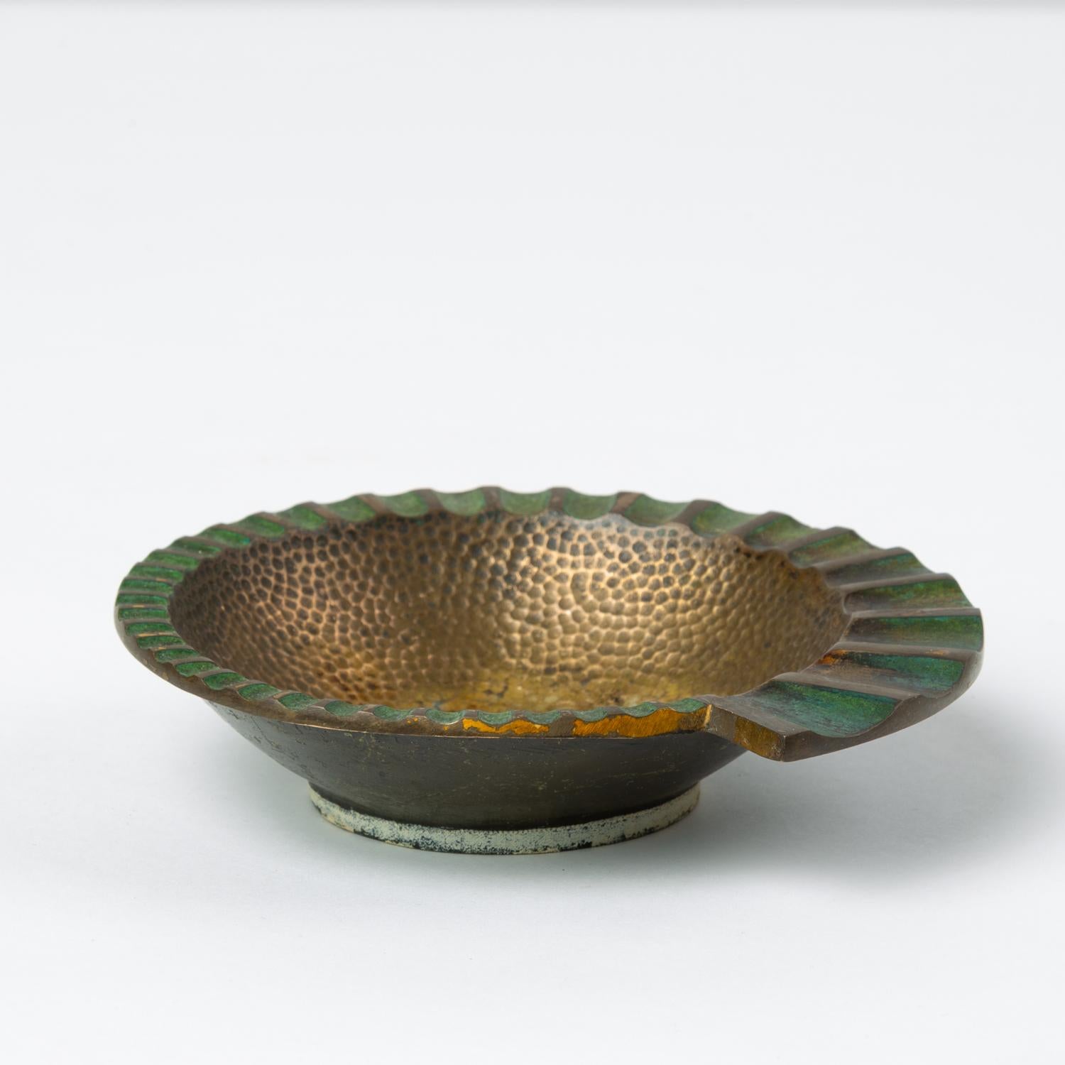 A heavy, cast bronze ashtray by Maurice Ascalon in a nautilus shape has a fluted, flat edge that widens as it spirals around the well, which has a hammered texture. The concave portions of the fluting are finished with a verdigris patina that