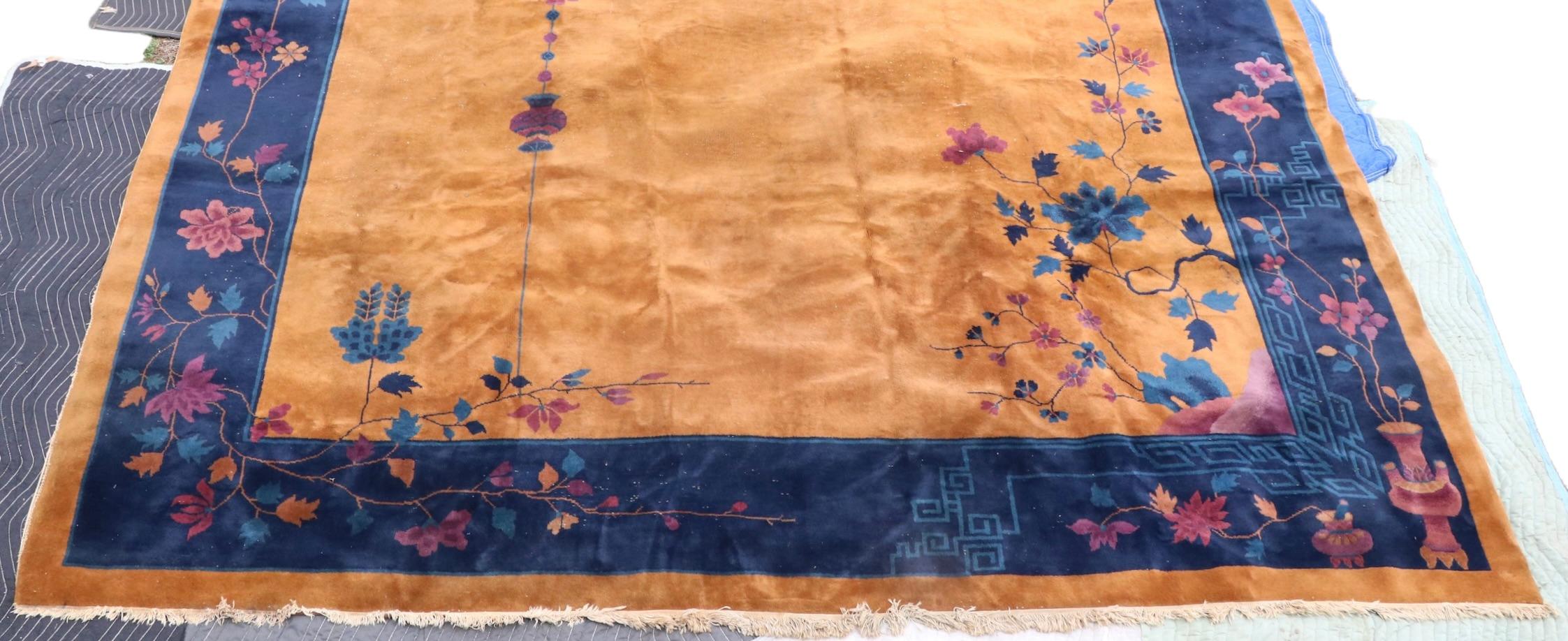 Spectaculaire tapis Art Déco de taille palace, datant des années 1920/1930. Le tapis présente un champ central de couleur beige ou moutarde, bordé de  bleu, puis moutarde à nouveau, il est orné d'un motif floral discret. La frange est en bon état,