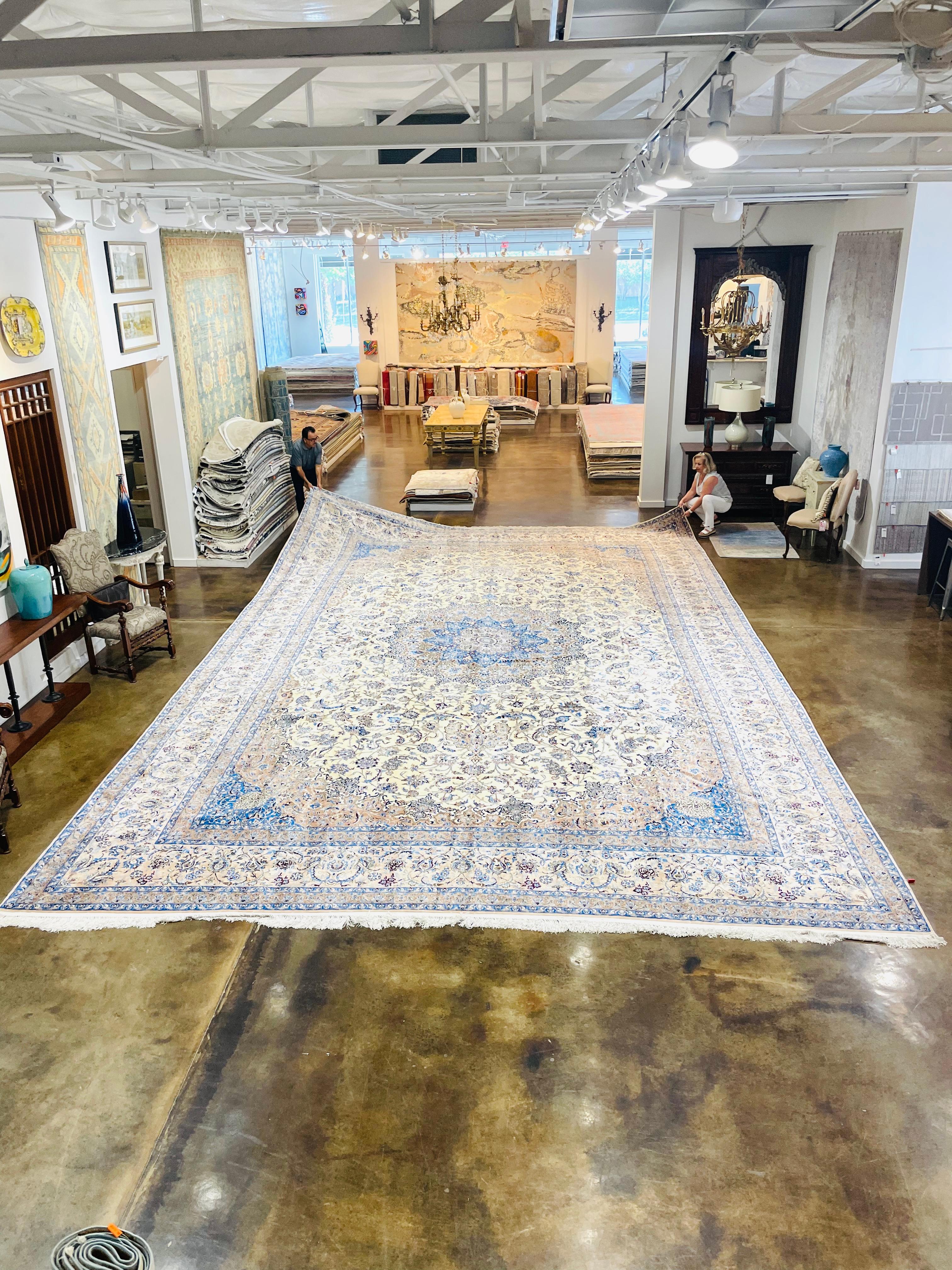 Ce magnifique tapis persan Nain de taille palace (17,1' x 27') est tissé dans une palette de couleurs délicates, avec des nuances d'ivoire, de bleu et de beige mises en évidence dans le motif floral et le médaillon central. Cette pièce est produite