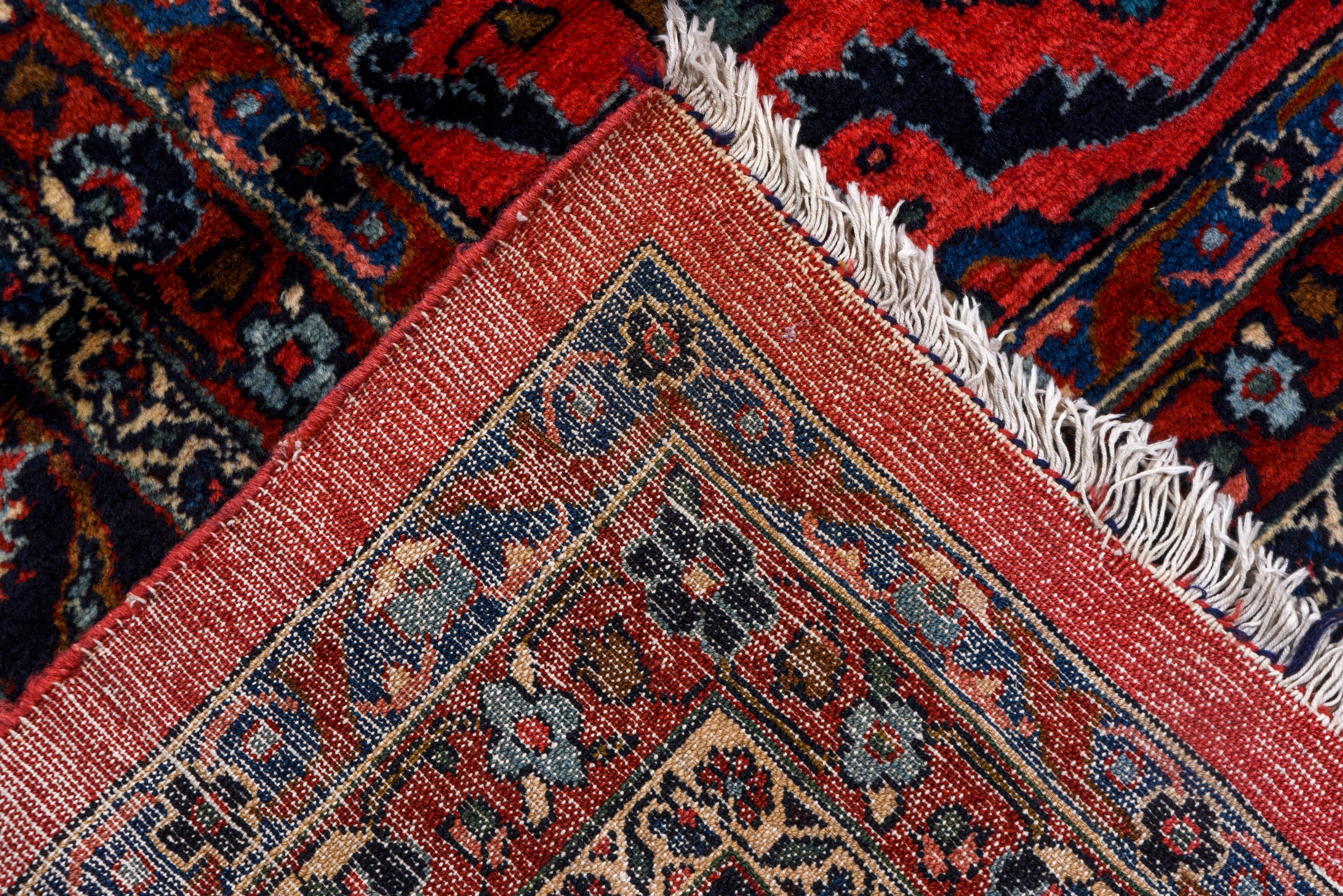 The gently abrashed rose-red field of this west Persian village carpet displays a floating, detached floral spray pattern highlighted in light and dark blues. The navy border of this 