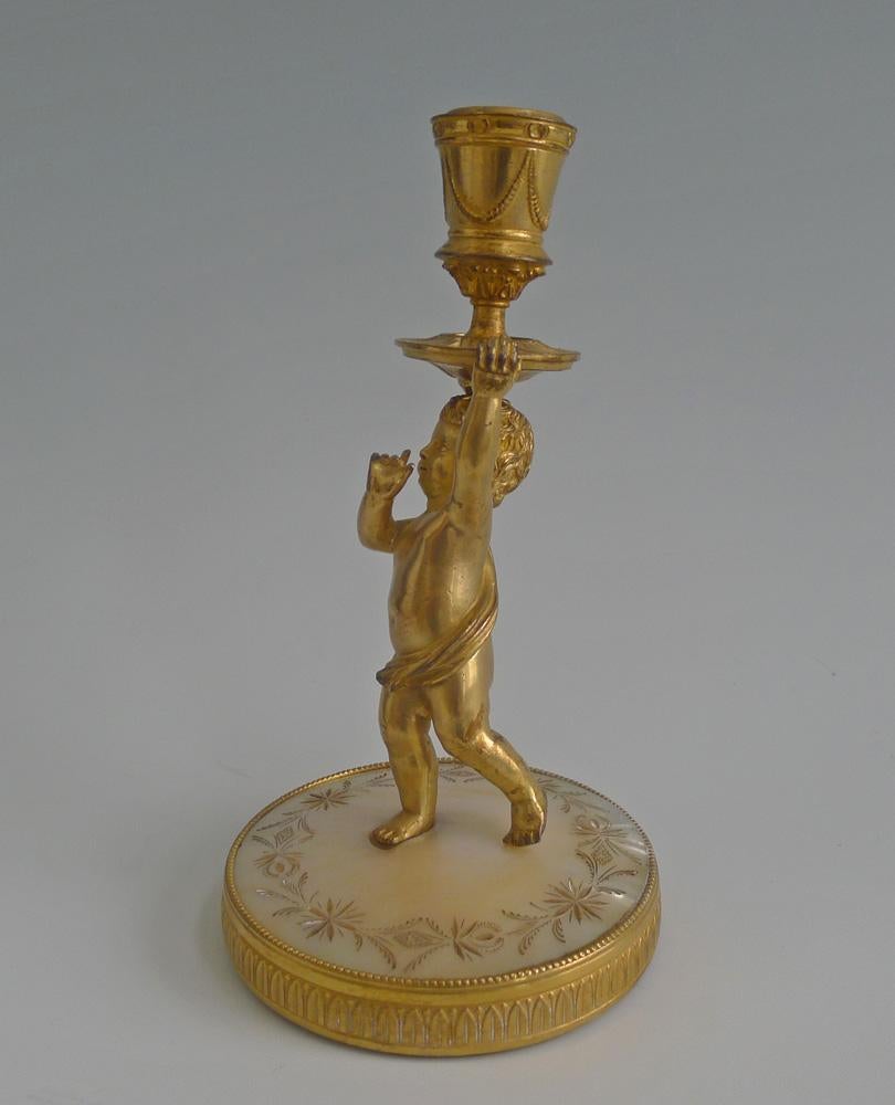 A fine Palais Royal piece of a putti or child, in fire, mercury gilded ormolu. The child stand over a finely engraved piece of mother of pearl, the patterns of flowers, garlands and diamond shaped designs. The base is a well-cast ring of ormolu