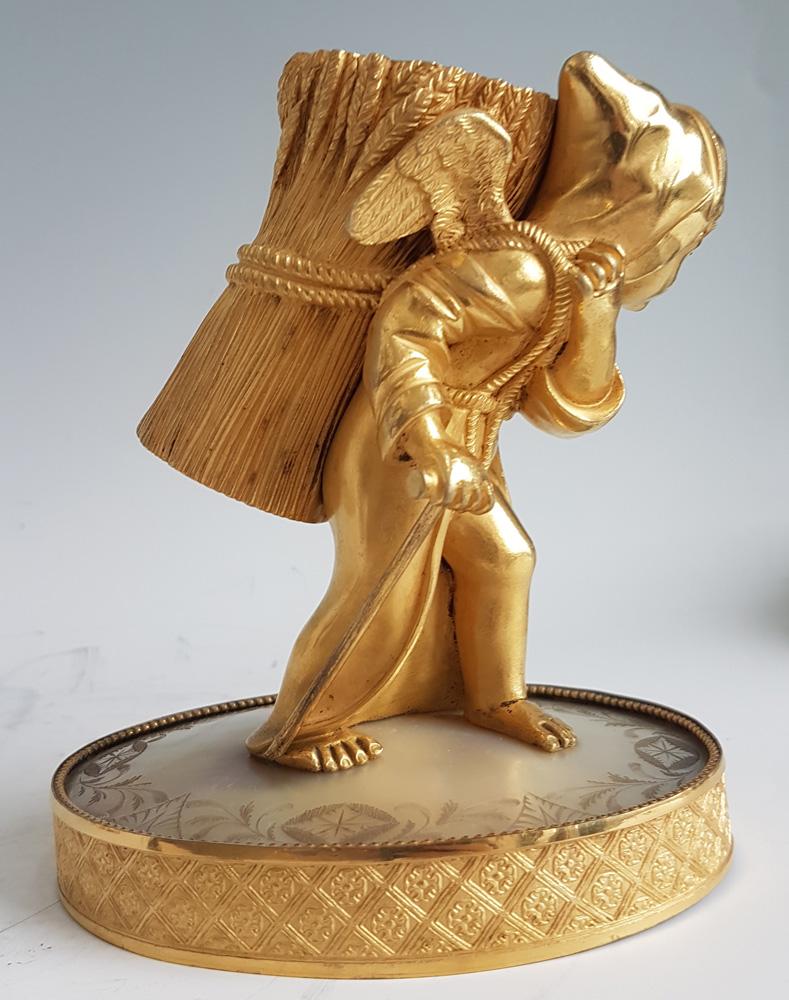 Palais Royal mother of pearl and ormolu taper holder. Modelled in the form of Cupid or a cherub, cloaked and hooded, as a monk, using a walking stick, and the taper holder on his back depicted as a sheaf of wheat. Set upon a fine ormolu base