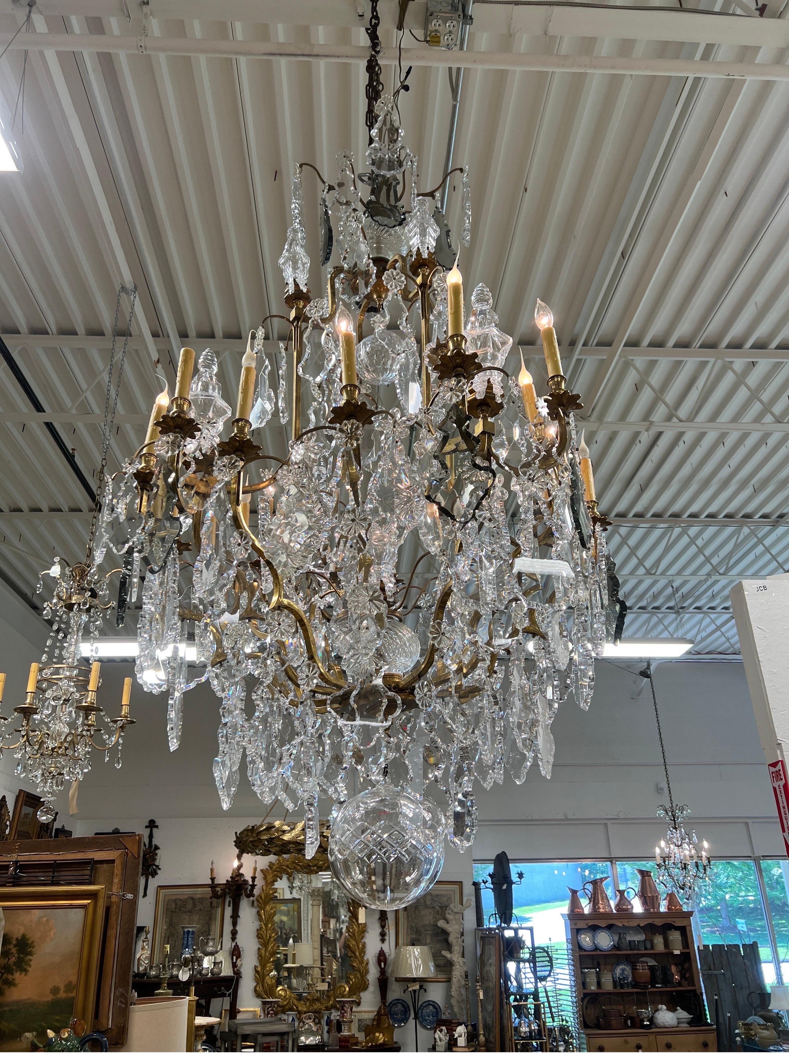 French, 19th century. This palatial antique Baccarat style chandelier is adorned with tremendous cut crystal prisms sizes ranging from 3.5-8.5” in clear and smokey glass. Large crystal newel post style finials are mounted across two tiers of the