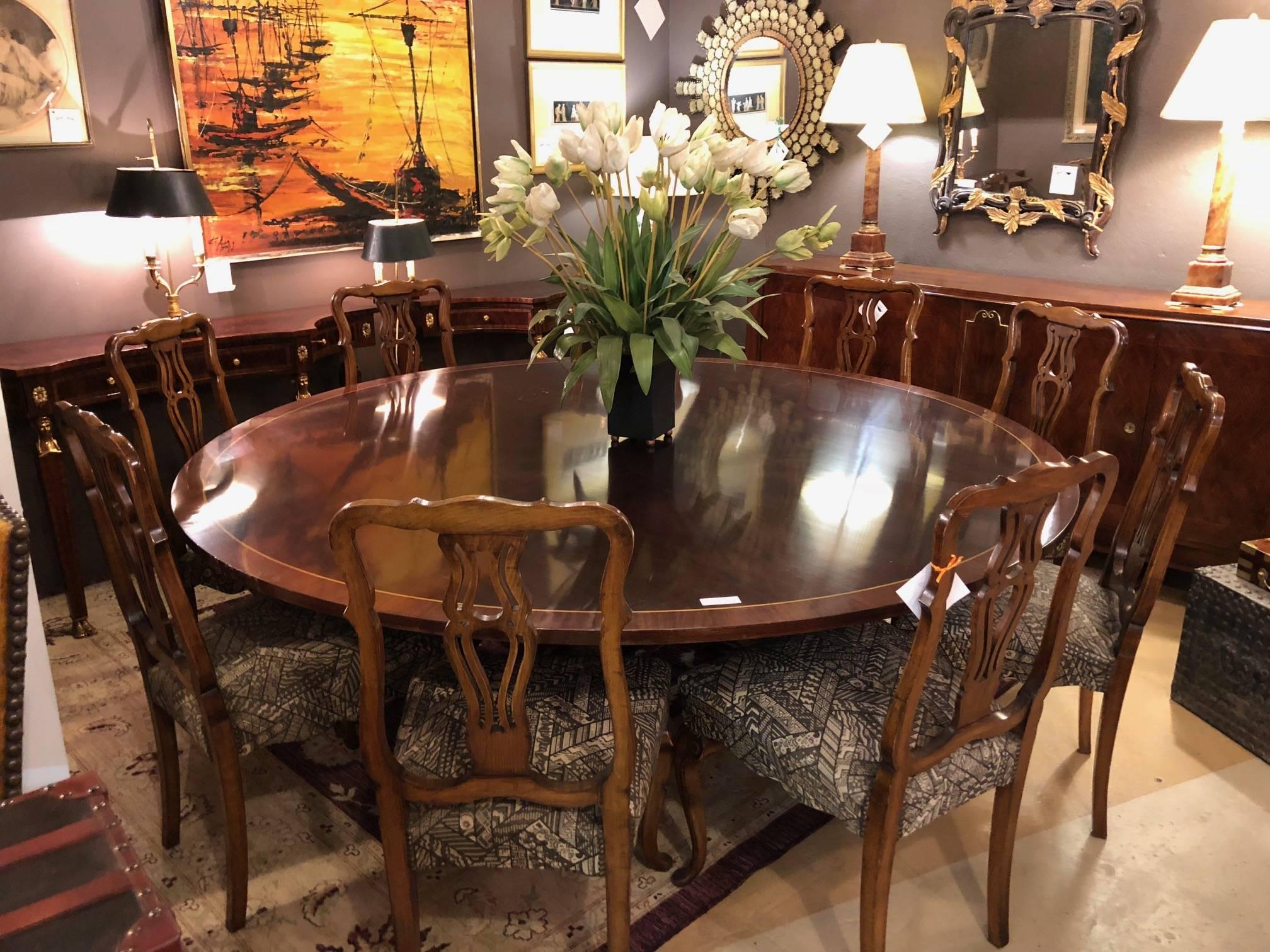 A custom quality palatial Georgian style banded flame mahogany circular dining table. This seven foot circular dining table has a fine flame mahogany grain with a think crossbanded satinwood edge sitting on scrolled column-form reeded legs.