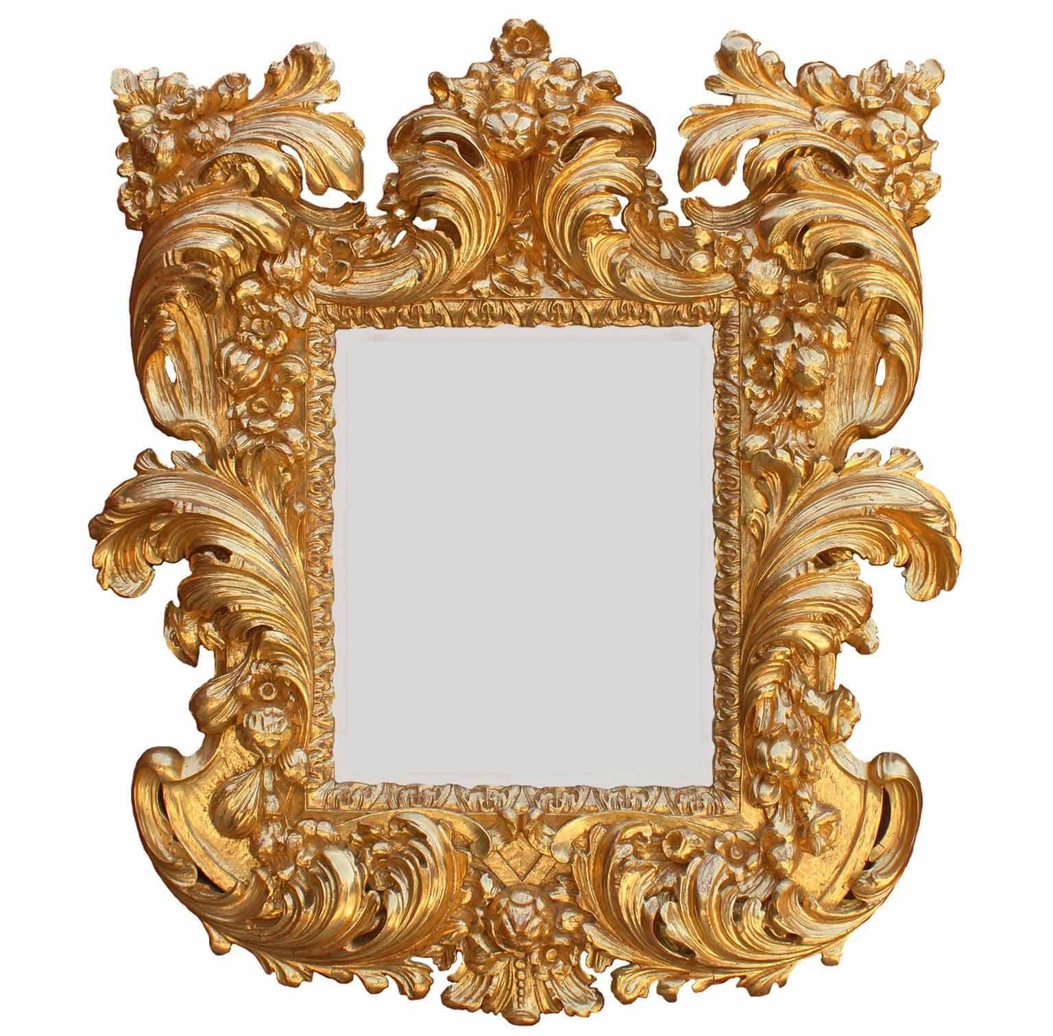 Ein feiner palastartiger italienischer Spiegelrahmen im Barockstil des 19. Jahrhunderts mit kräftigen Schnitzereien aus Florentiner Goldholz. Der kunstvoll geschnitzte Rahmen mit Schriftrollen, Akanthus, Früchten und Blumenmuster ist mit einer