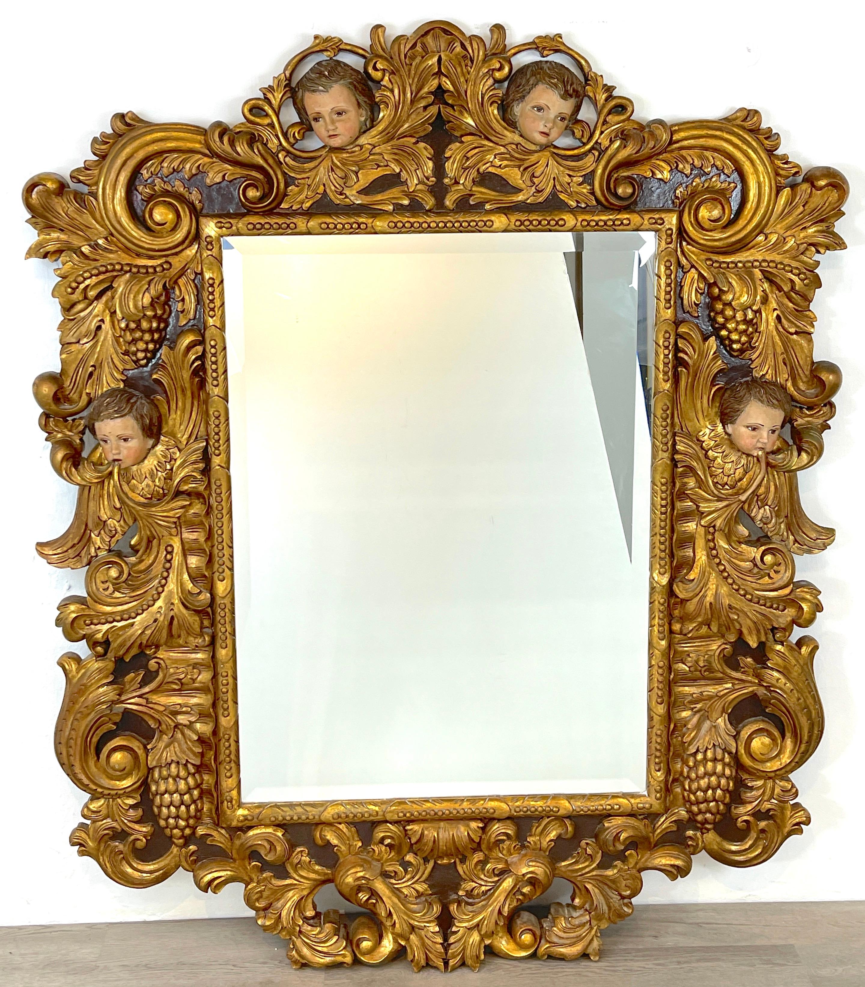 Palatial Italian carved figural giltwood & polychromed Baroque style mirror, with four carved putti heads with inset glass eyes, amongst giltwood foliate background. With inset 43