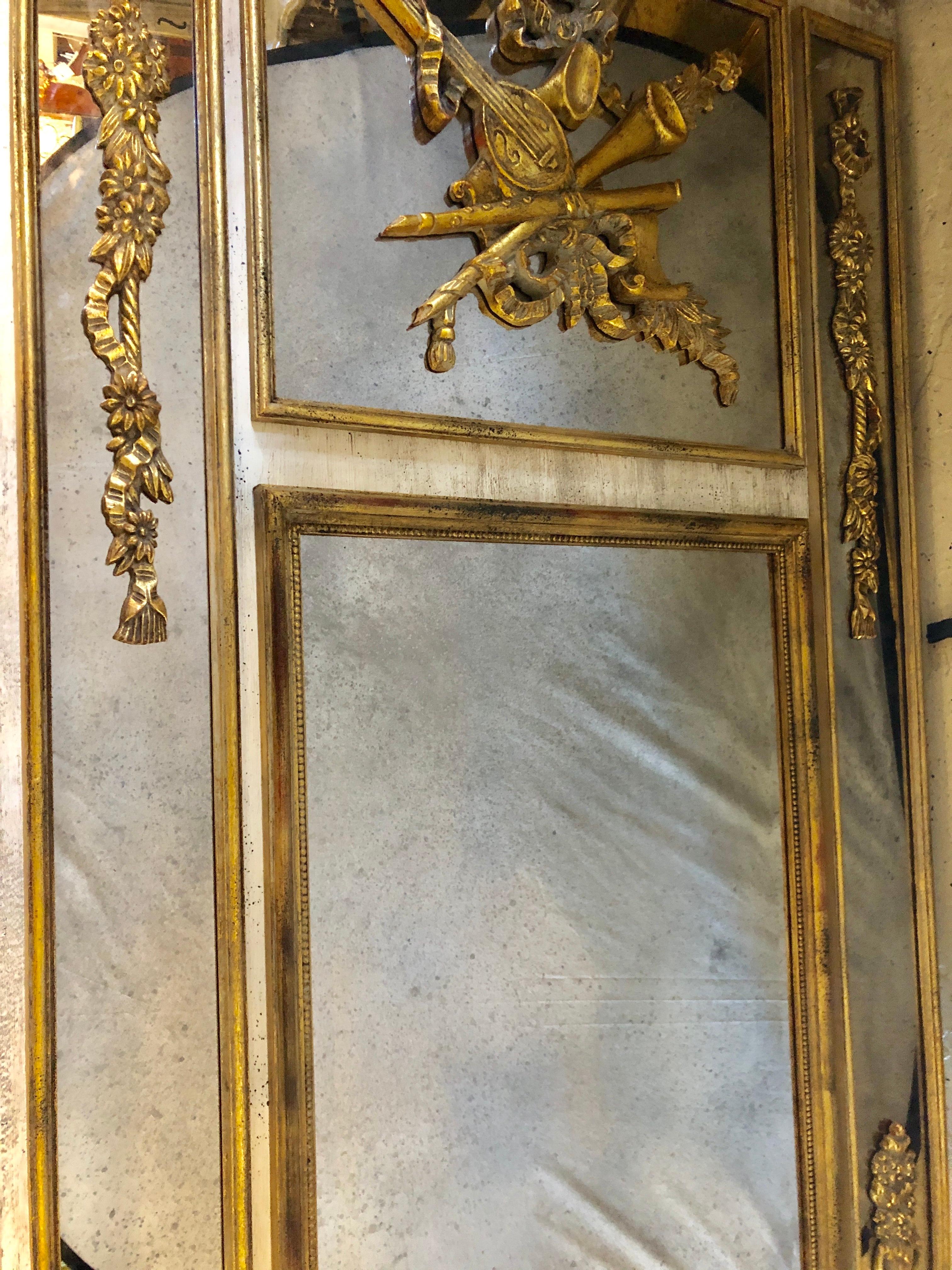 A large and impressive Louis XVI style gilt and poly chromed wall / mantle or console mirror having gilt relief with carved musical motif applique framing the beveled center mirror.