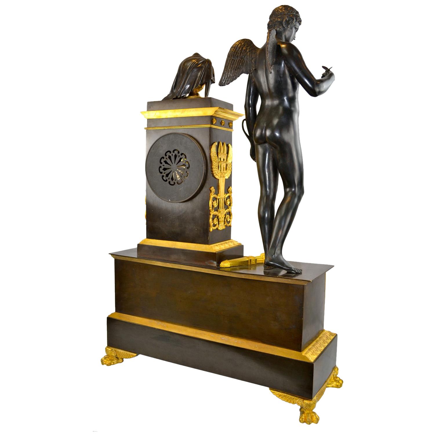 Pendule de cheminée de la fin de l'Empire français, d'échelle palatiale, représentant Cupidon et Eurydice. La base rectangulaire en bronze patiné repose sur quatre pieds en forme de pattes de lion et présente une frise dorée sur tout le devant,
