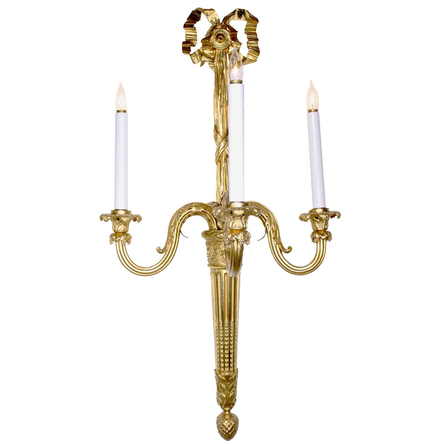 A Palatial Set of Four French 19th-20th Century Louis XVI Style Neoclassical Gilt-Bronze Three-Light Wall Lights (Sconces). The tall elongated ormolu sconces with a back plate in the form of a torch, each issuing three scrolling candle-arms,