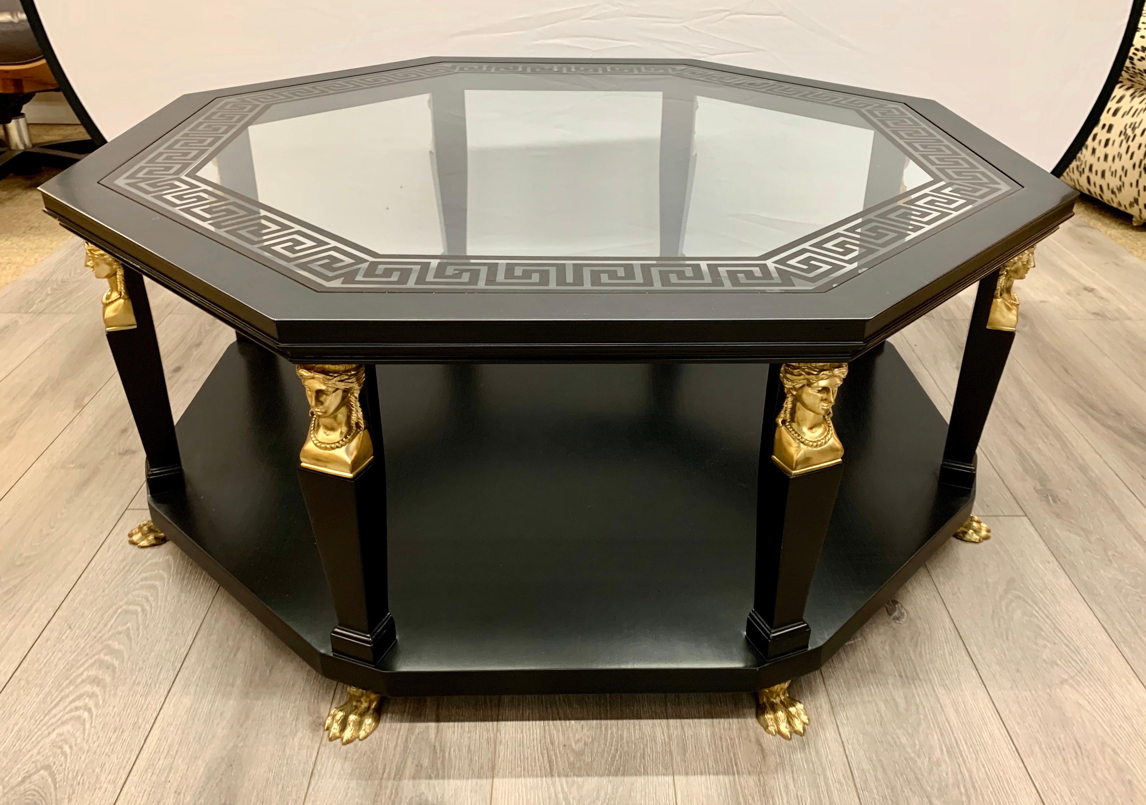 Elegant black and gold Versace-style cocktail table that had luxurious black and gold color as well as etched Greek key design on glass top. Features all brass feet and appliques.