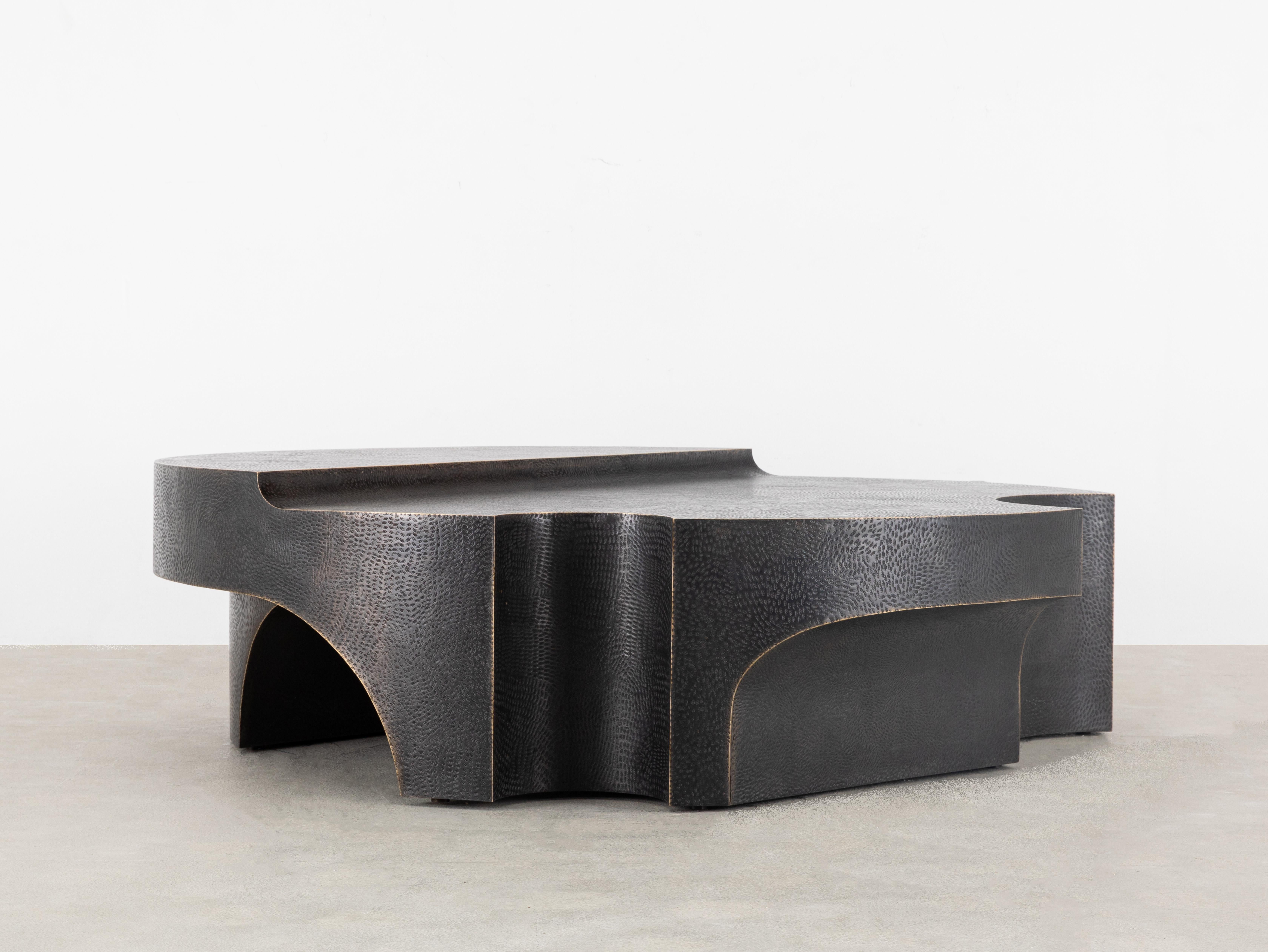 Inspired by the architecture style of the Italian Renaissance, this sculptural coffee table is crafted in brass by welding together several hammered, textured sheets of metal. The softness of the curves is juxtaposed with the linearity of the coffee