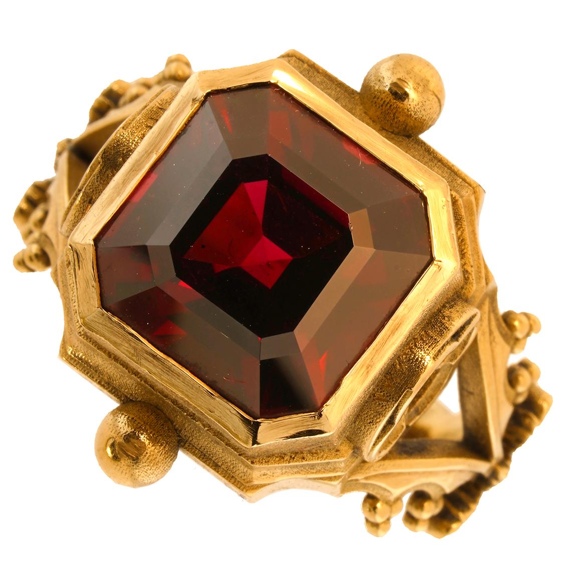 Intricately handcrafted in 9kt yellow gold this exquisite signet ring features a mesmerizing scarlet 13mm x 13mm Asscher cut garnet suspended like the deep hues of an oil painted ceiling above an ornate gothic gallery. Adorned with quatrefoil
