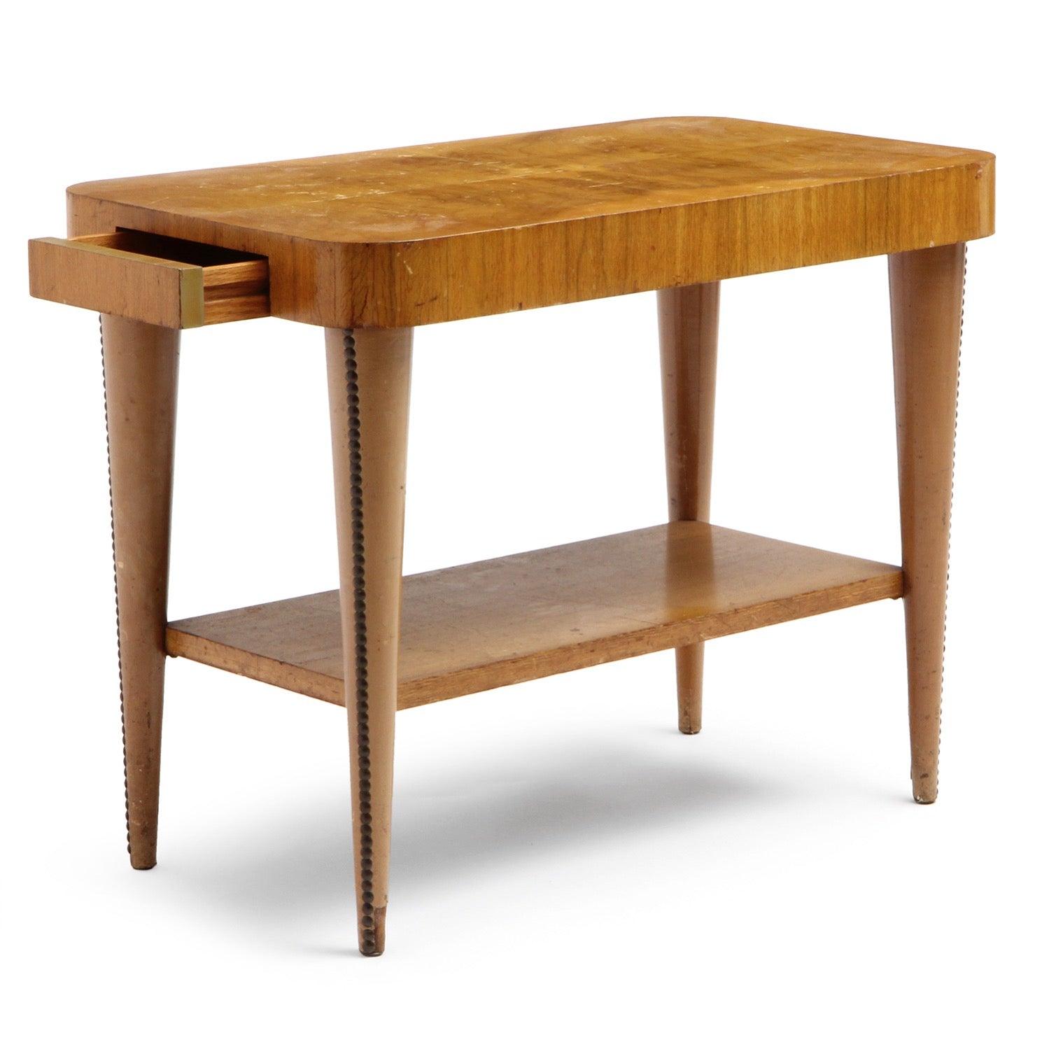 Mesa auxiliar con estante inferior y patas tachonadas y ahusadas forradas de polipiel, tablero revestido con cuadrantes de burl de acacia a juego con los libros.