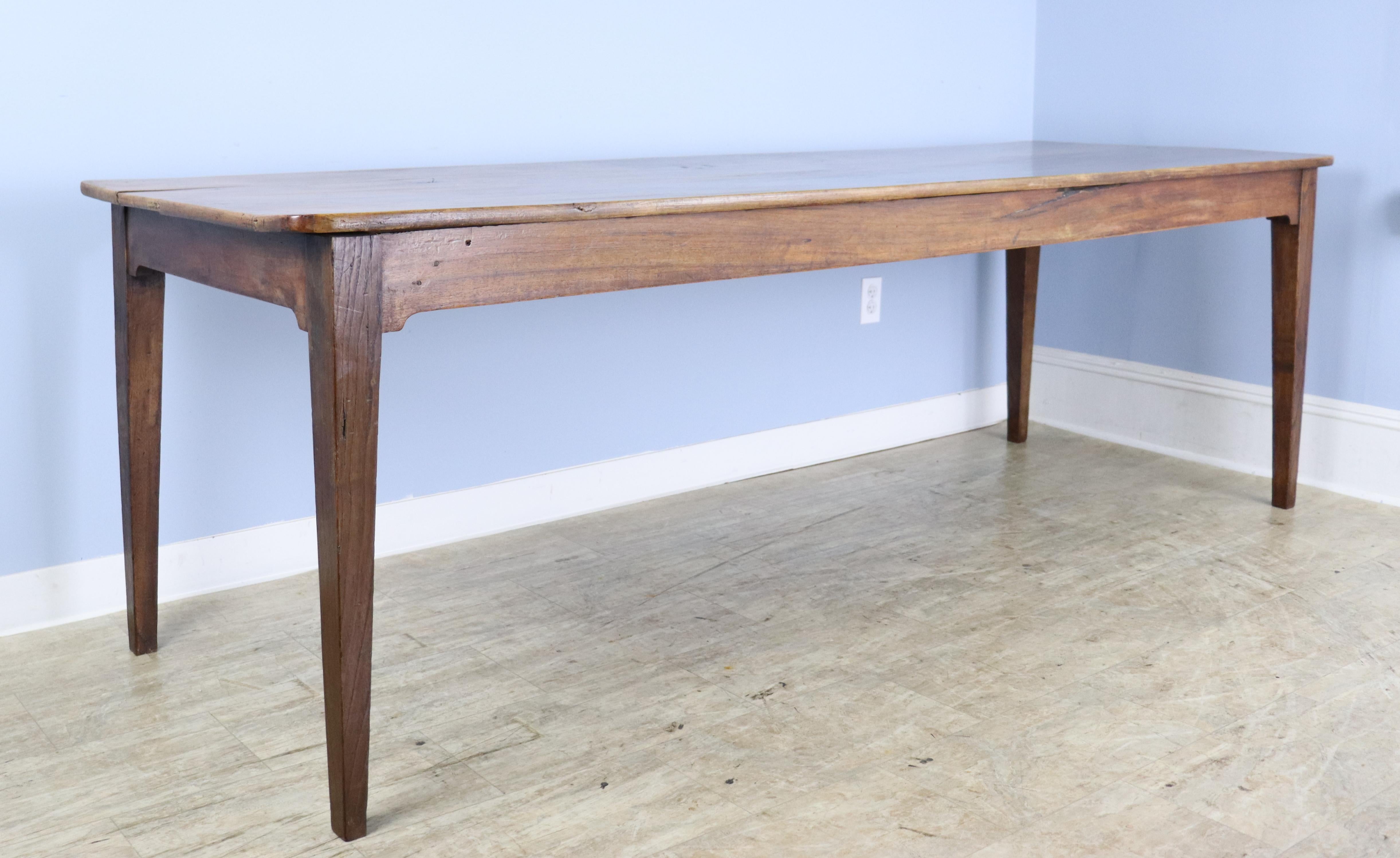 A very pretty long slim pale walnut farm table.  The original walnut legs have been replaced with a rich brown chestnut which complements the walnut.  The top is quite clean and has nice grain and good patina.  The generous apron height of 25.75