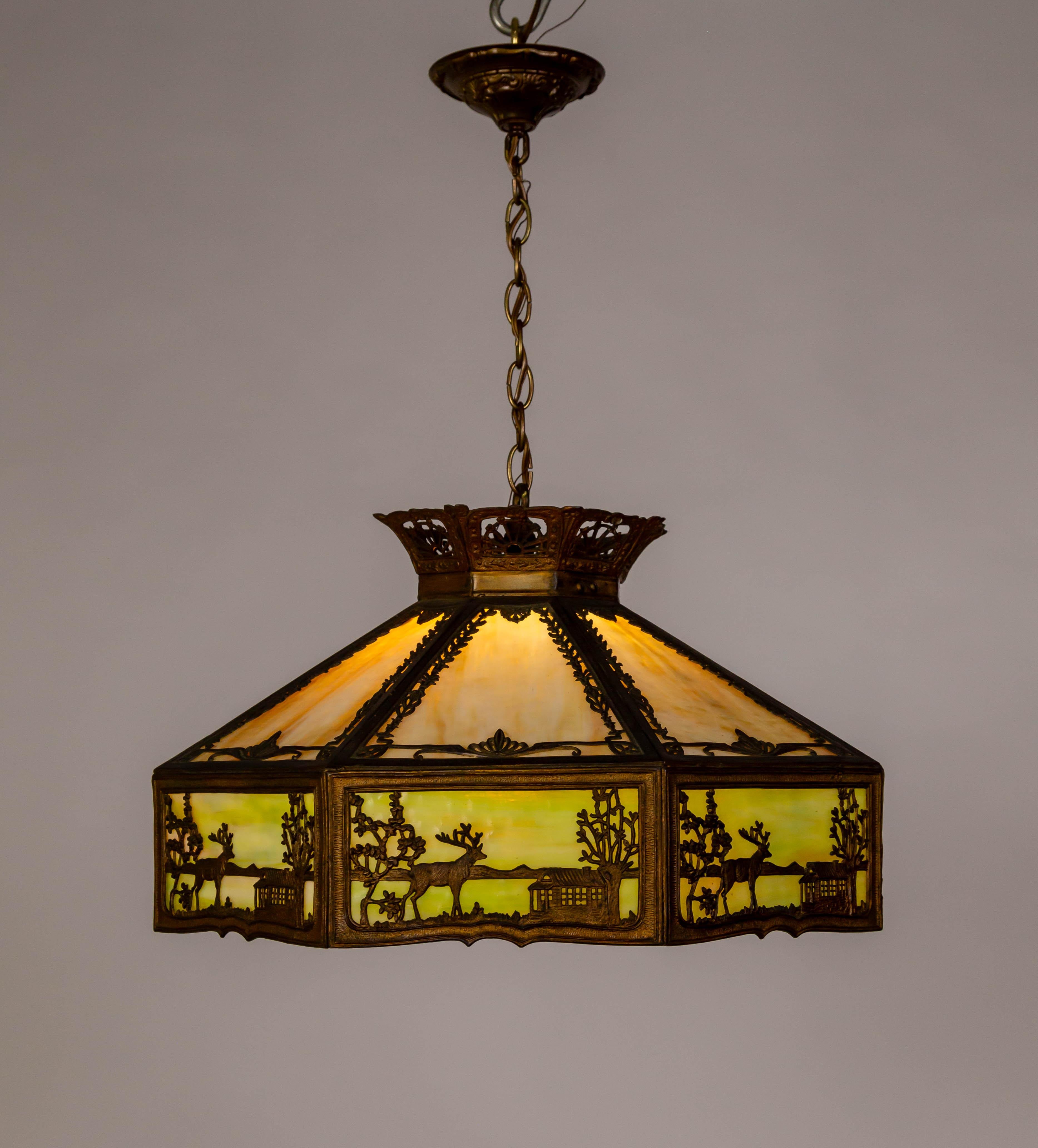 Una detallada lámpara colgante geométrica de cristal de escoria en forma de paraguas de principios del siglo XX. El vidrio de escoria es de color ámbar pálido abigarrado y amarillo verdoso, con un marco de tonos bronce. Los paneles laterales