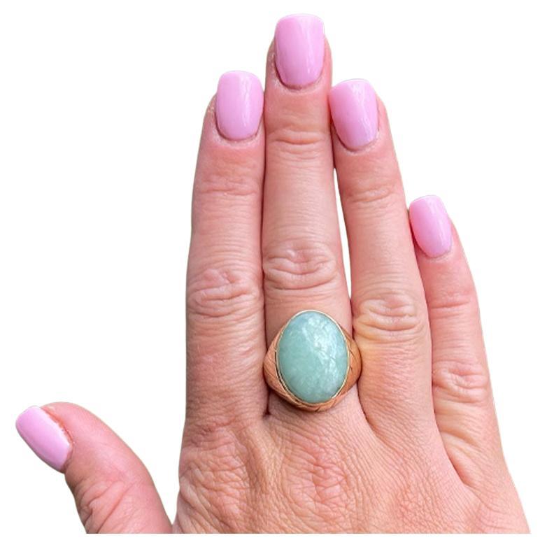 Pale green oval cabochon cut jade ring, bezel set in 14k yellow gold. The Jade measures approximately 19.86 mm x 14.64 mm x 5.24 mm with an estimated weight of 13.74 carats. The shoulders have textured diagonal stripes and high polish finish
