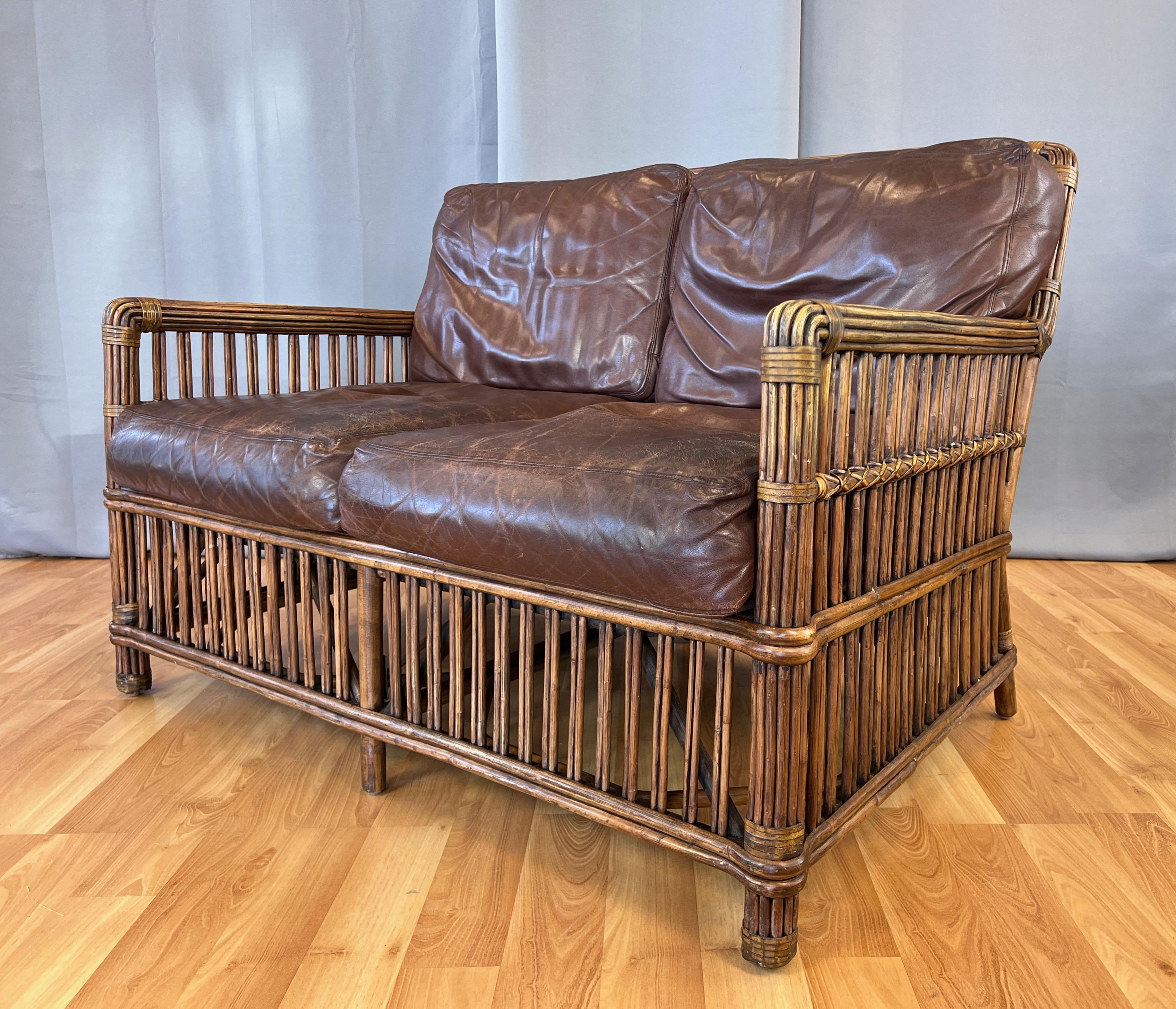 A very handsome and hard to find earlier version of Palecek’s Art Deco-style rattan and leather President’s loveseat or two-person sofa. 

Unlike the currently available version that has integrated magazine racks and cupholders on the arms, this