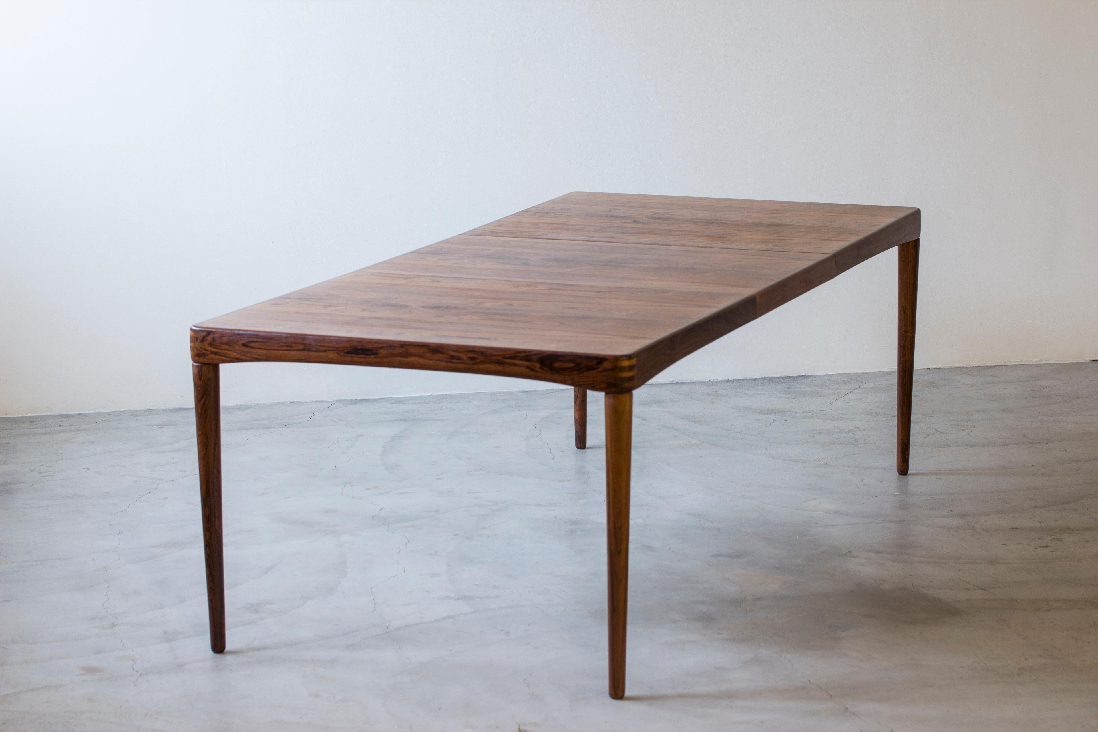 Dining table designed by Henry Walter Klein. Produced in Denmark by Bramin during the 1950s. Excellent book matched rosewood/palisander veneers with articulate grain shifting in dark brown and black. Solid rosewood in the tapered legs and edges.