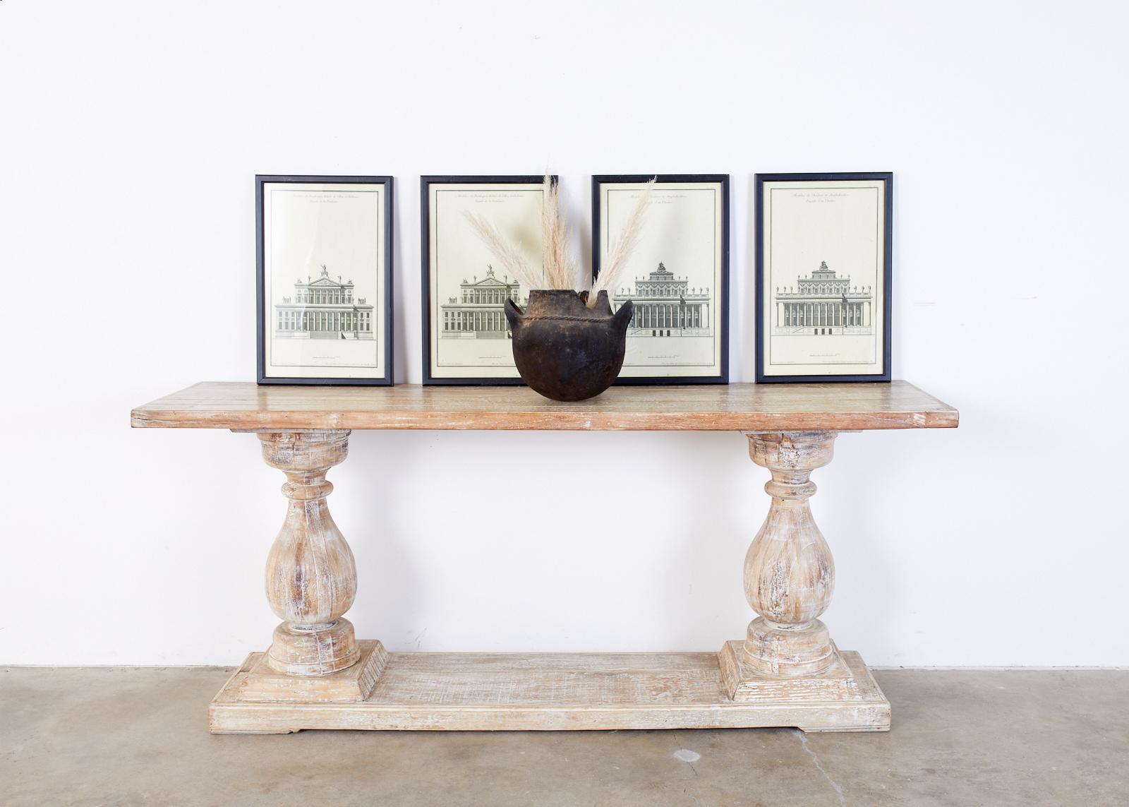 Palladian style 21st century baluster console table or sofa table featuring a stylish Cerused or bleached oak finish with an aged patina. The plank top is supported by two thick baluster shaped pedestals mounted to a stepped base. The lovely finish